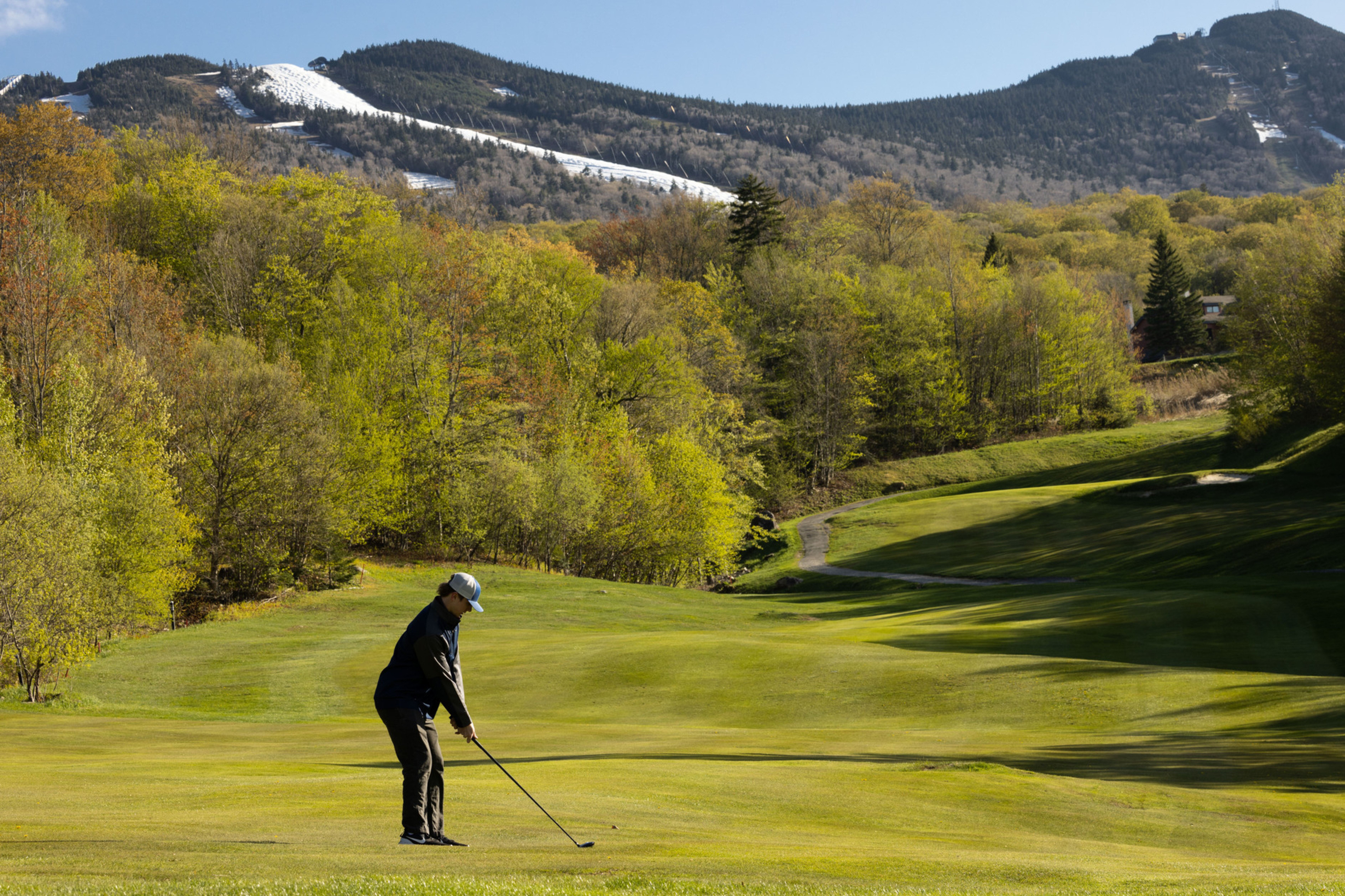 A golfer prepares to swing on a lush green course with mountains in the background.