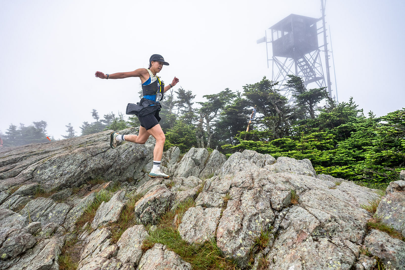 A runner navigates rocky terrain in misty conditions, with a lookout tower in the background.