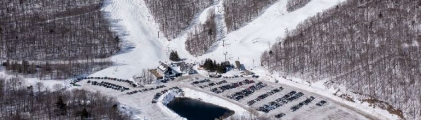 Aerial view of snow-covered ski slopes and a parking lot at a ski resort.