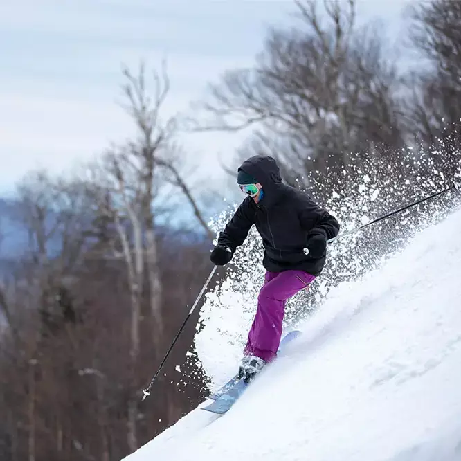 A skier in a black jacket and purple pants descends a snowy slope at Killington Mountain.