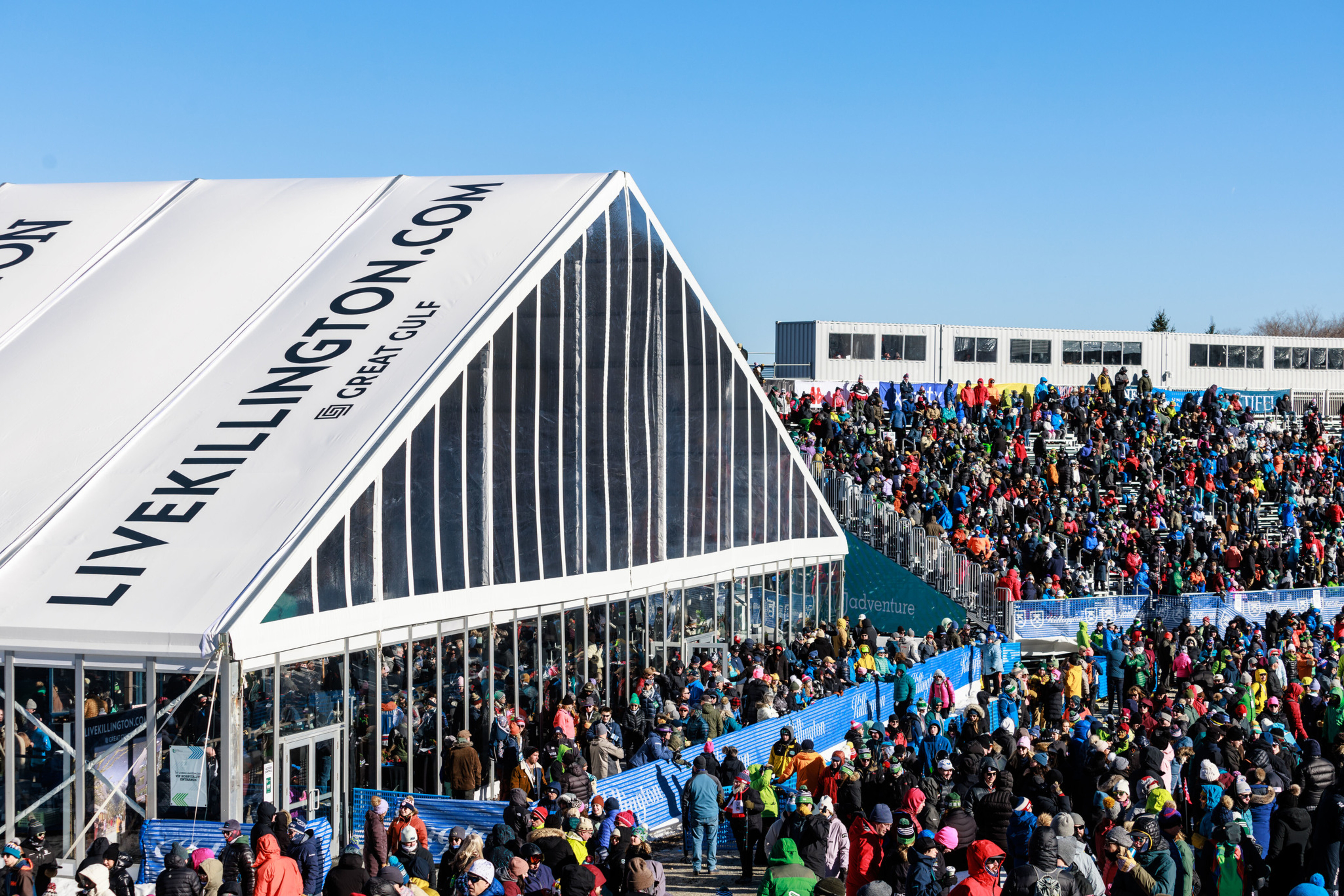 Crowd gathered outside a large tent at a winter event, with clear blue skies above.
