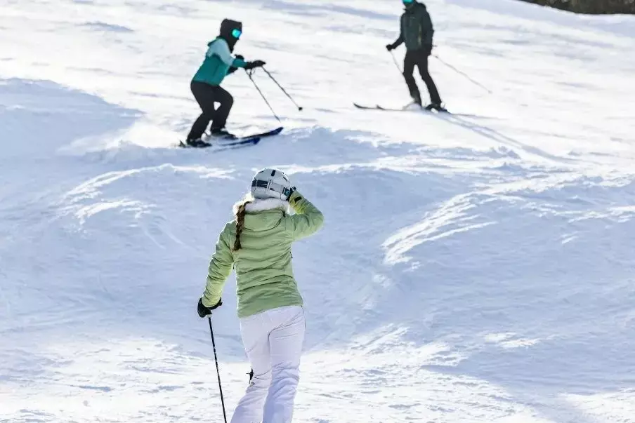 Three skiers navigate a snowy slope on a bright, clear day.