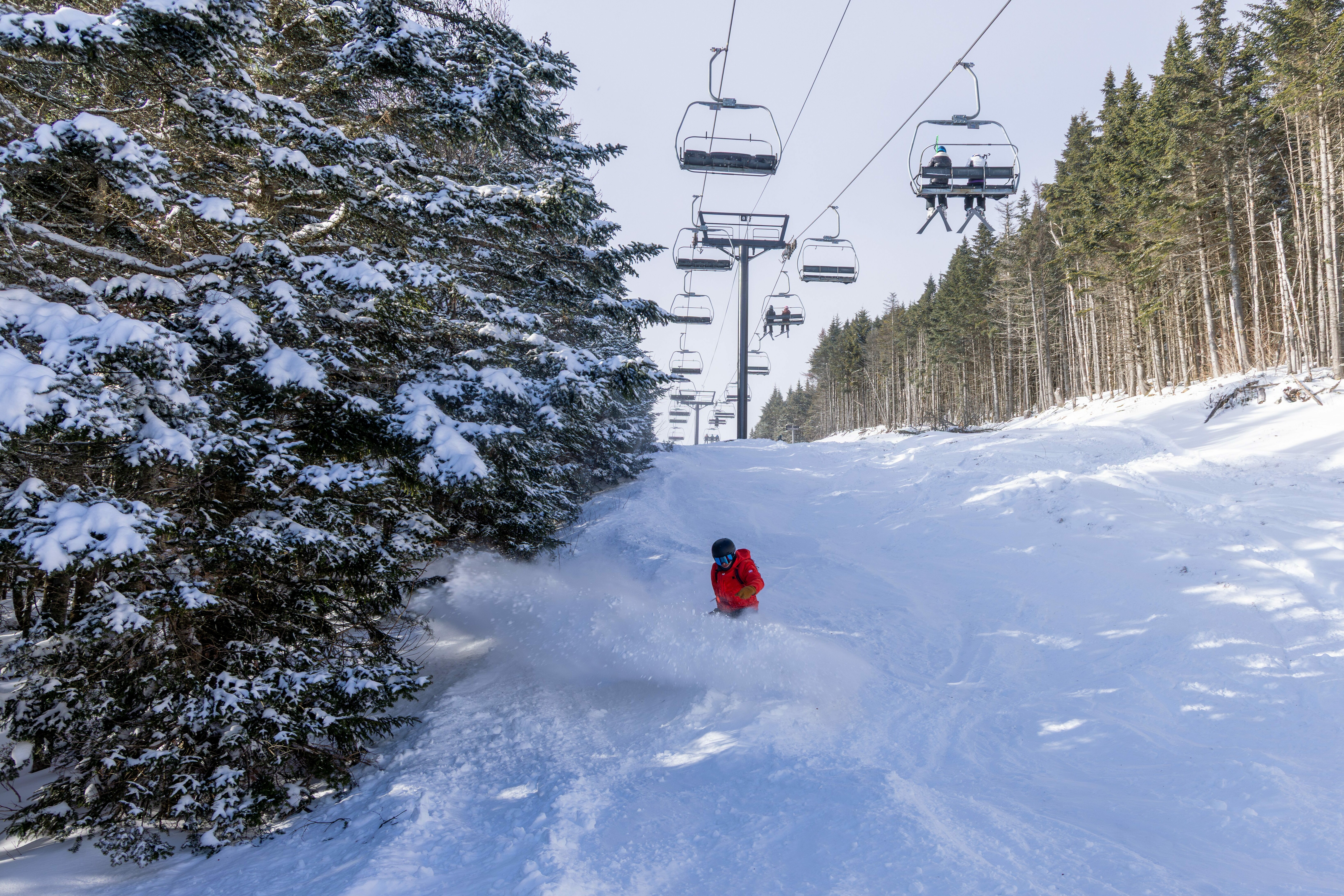 A skier in an orange jacket carves through snowy terrain with ski lifts above.