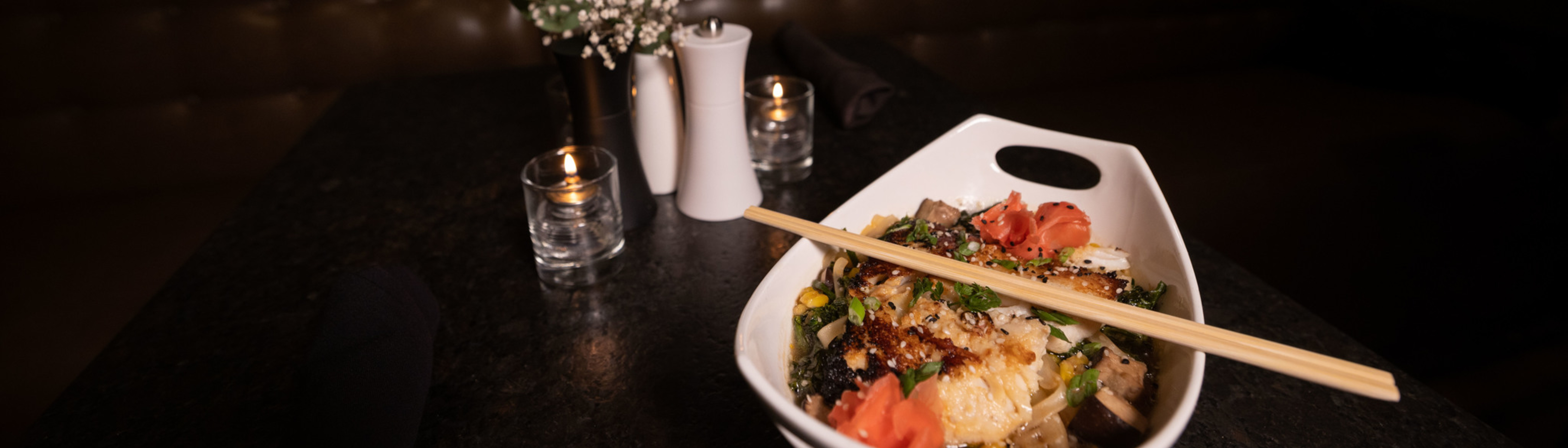 A bowl of colorful sushi with chopsticks, surrounded by soft lighting and decor.
