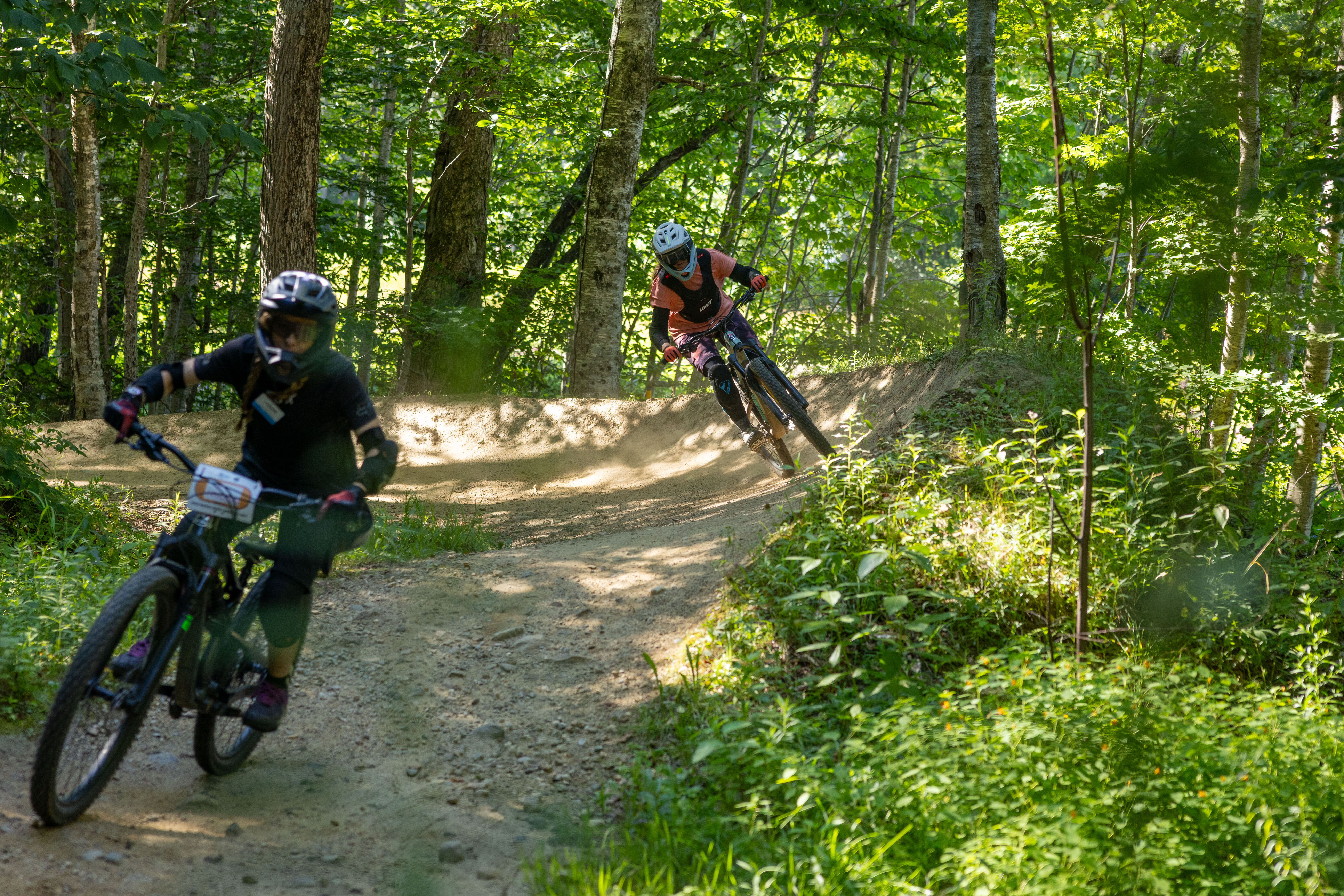 Two mountain bikers navigate a dirt trail in a lush green forest.
