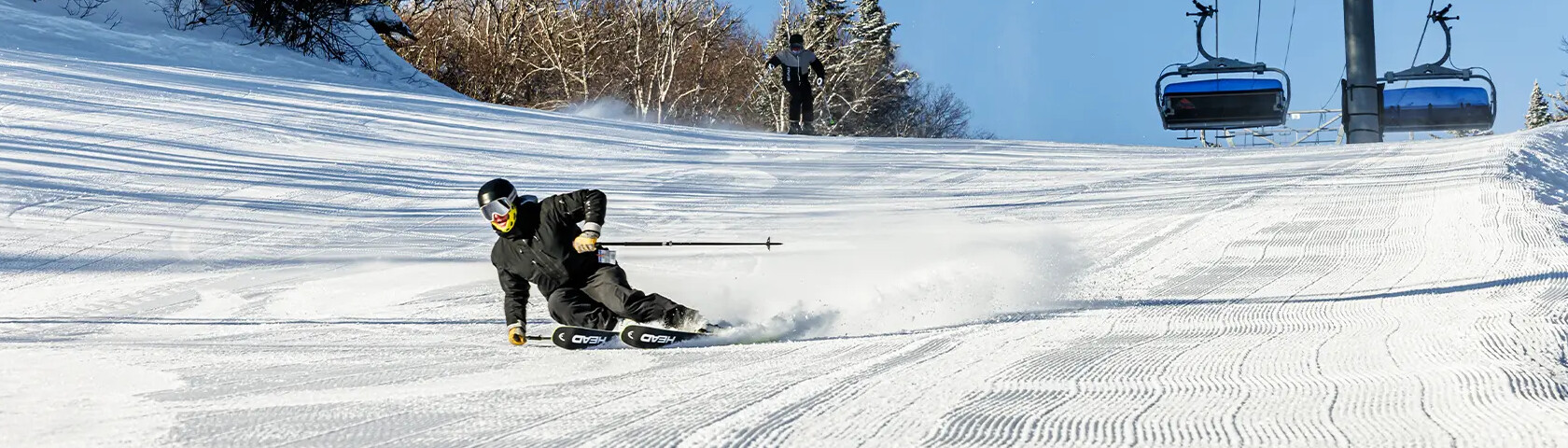 Skier carving through snow on a slope with a ski lift in the background.