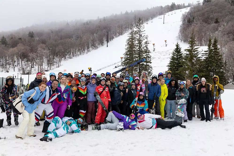 A large group of people in colorful ski gear poses in a snowy mountain landscape.
