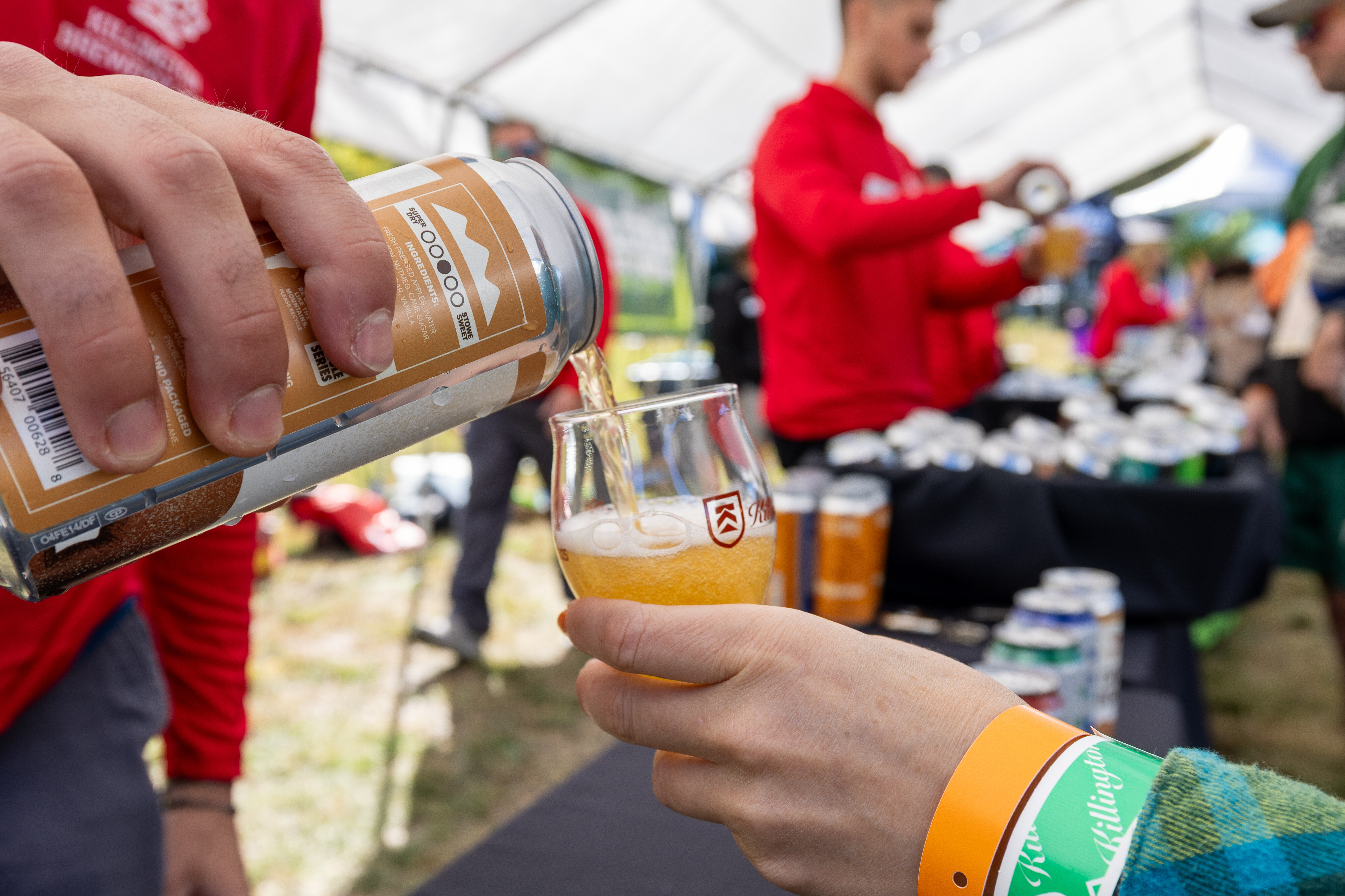 A hand pours beer from a can into a glass at a festival.