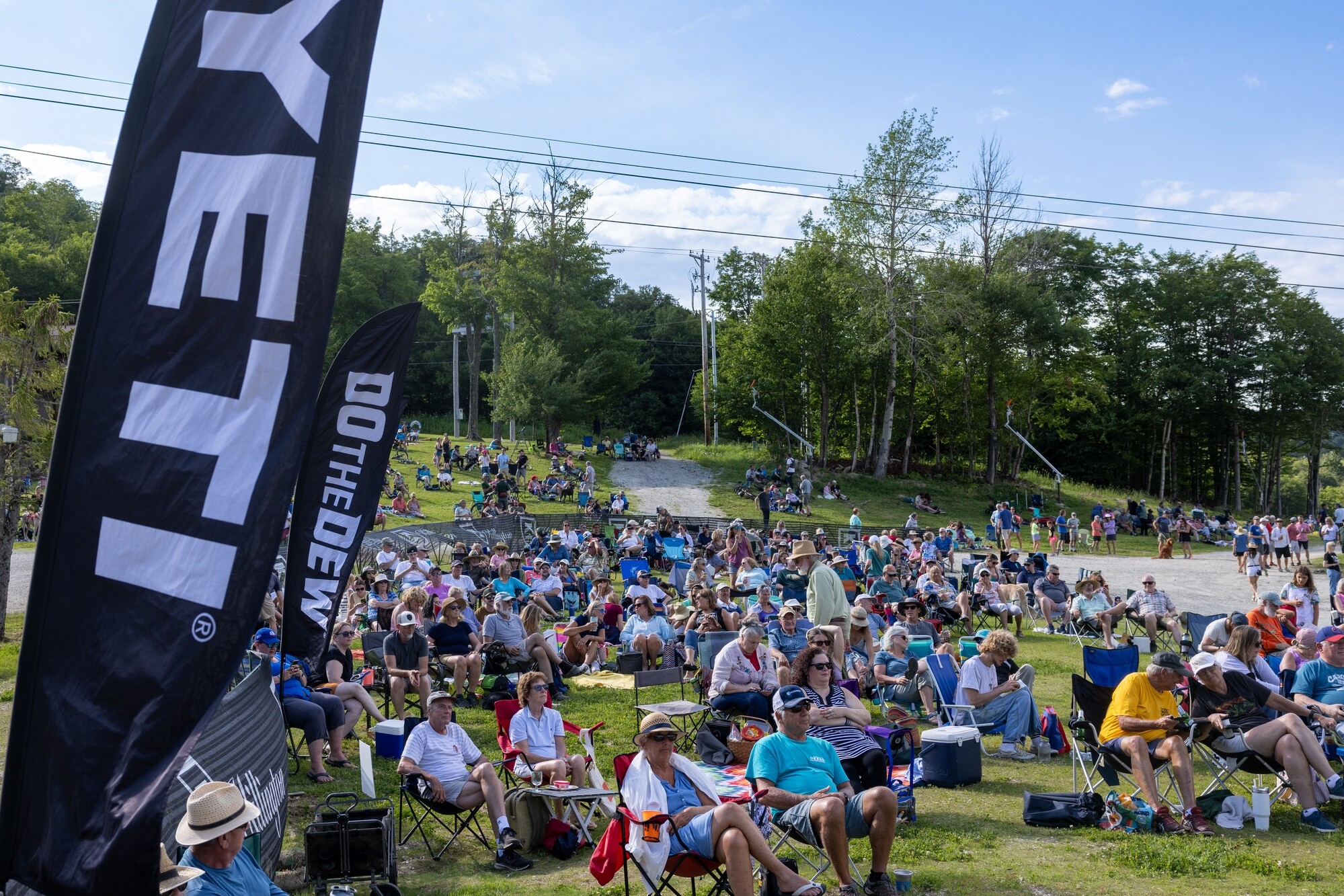 Crowd of people seated on grass for an outdoor event, with flags in the foreground.