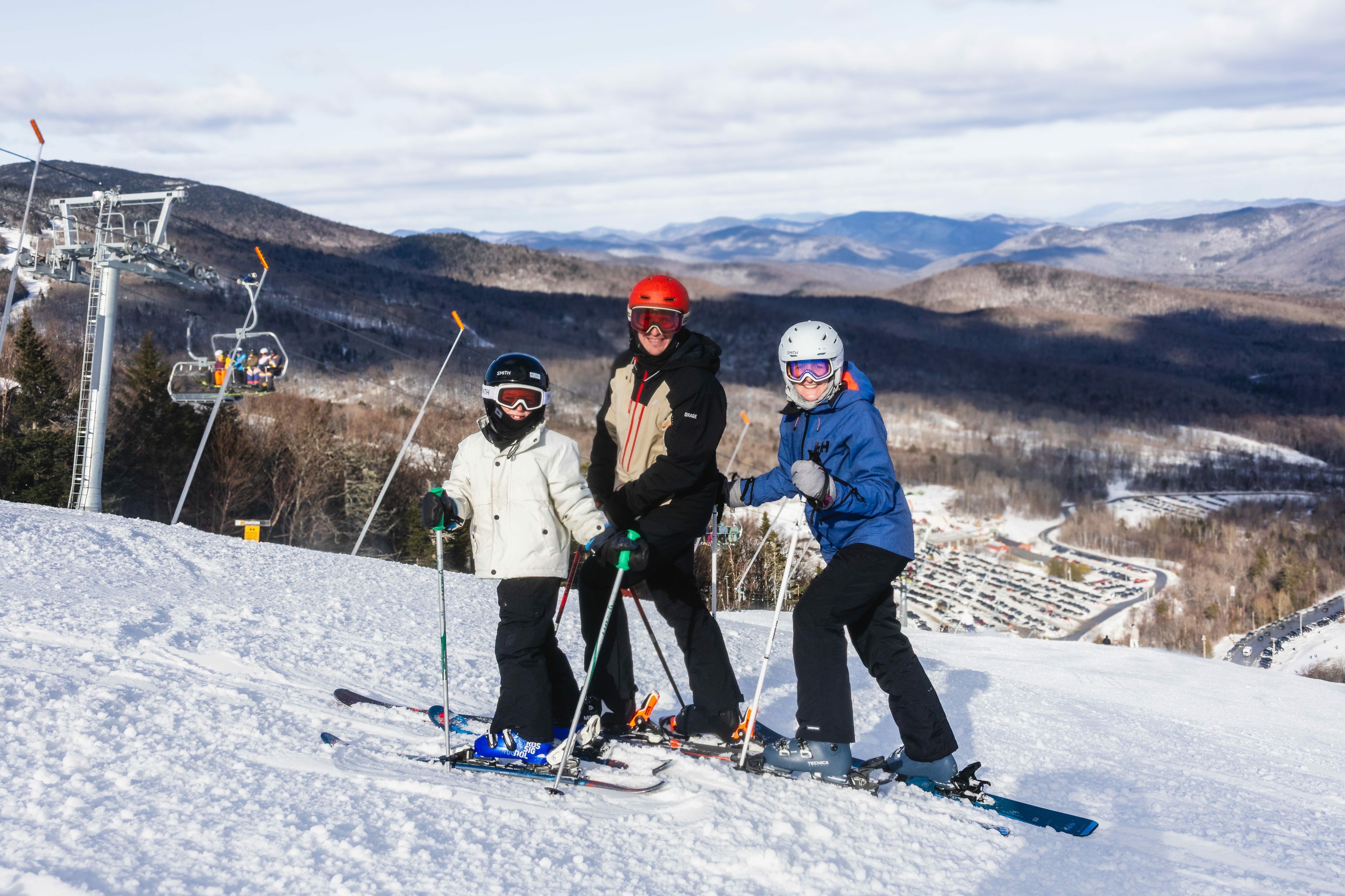Three skiers pose together on a snowy slope, with mountains and a ski lift in the background.
