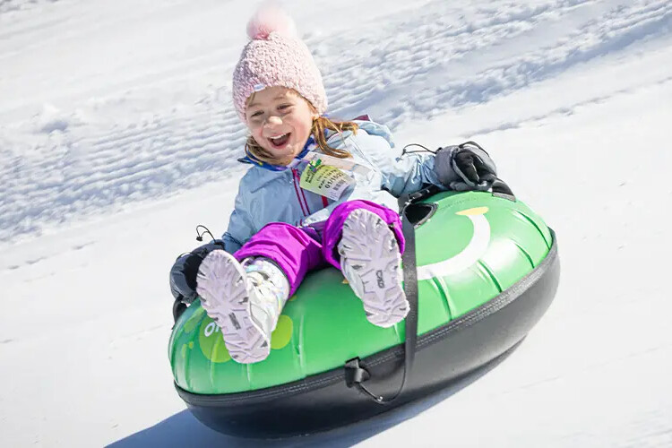 A joyful child sledding down a snowy hill on a green inflatable tube.