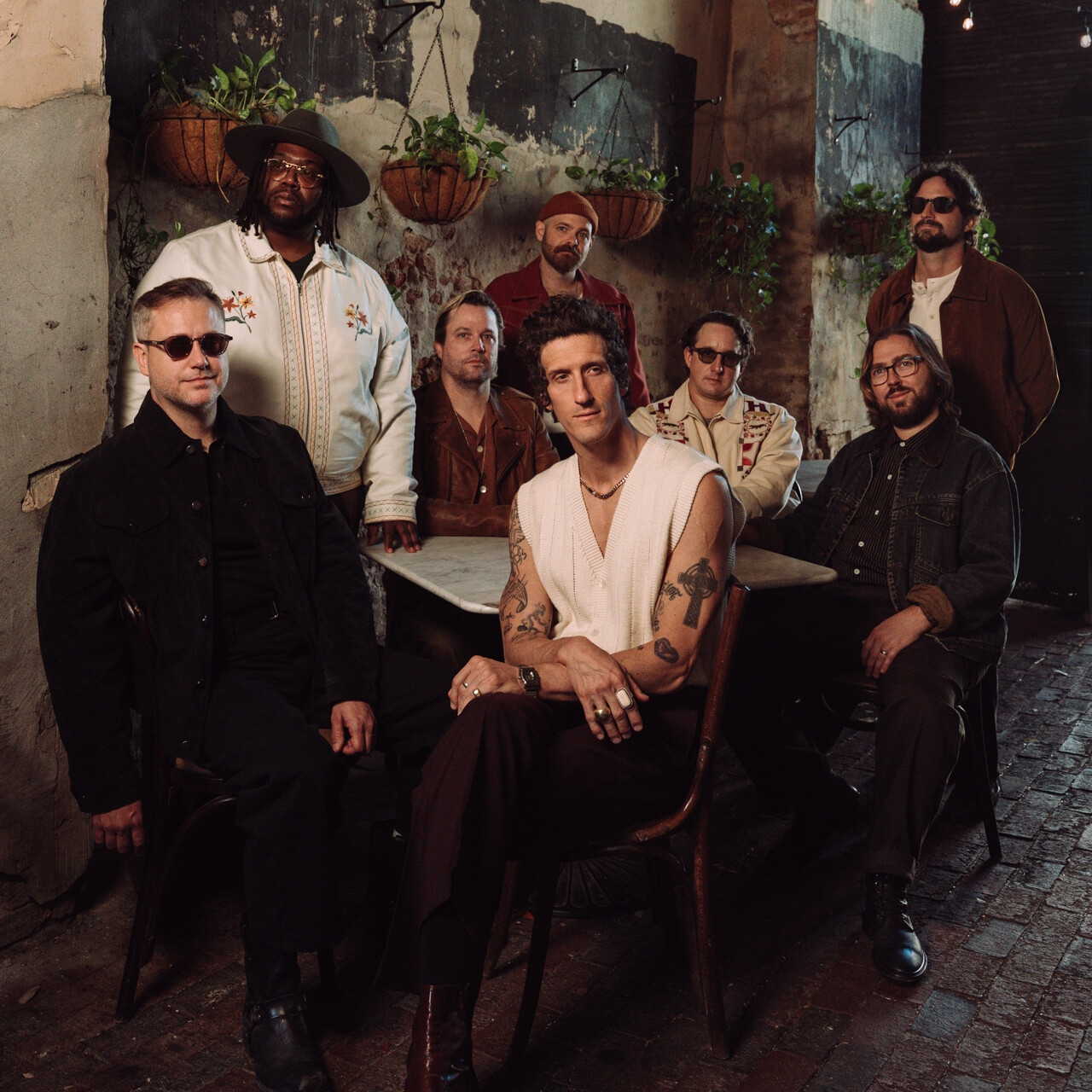 A group of eight men poses together in a rustic setting.