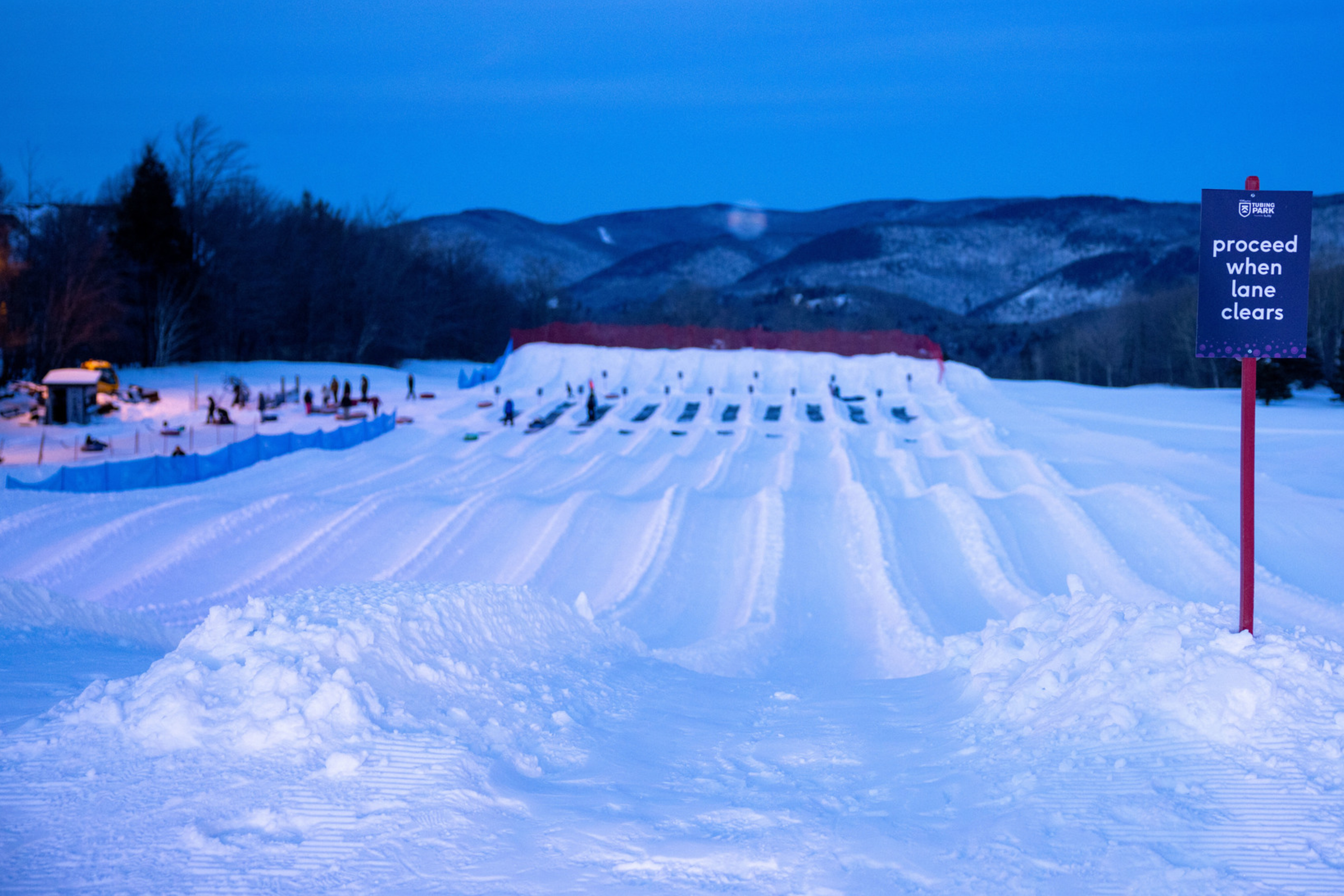 Snow tubing slope at dusk with a sign indicating to proceed when lanes clear.