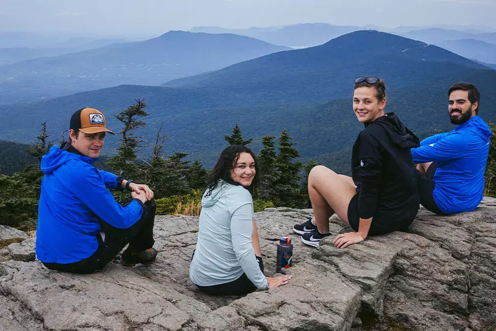 Four hikers sitting on a cliff, overlooking a mountainous landscape.