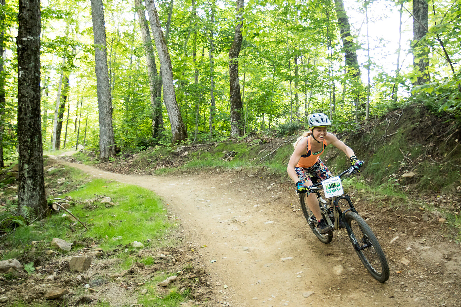 A female cyclist navigates a dirt trail through a lush, green forest.