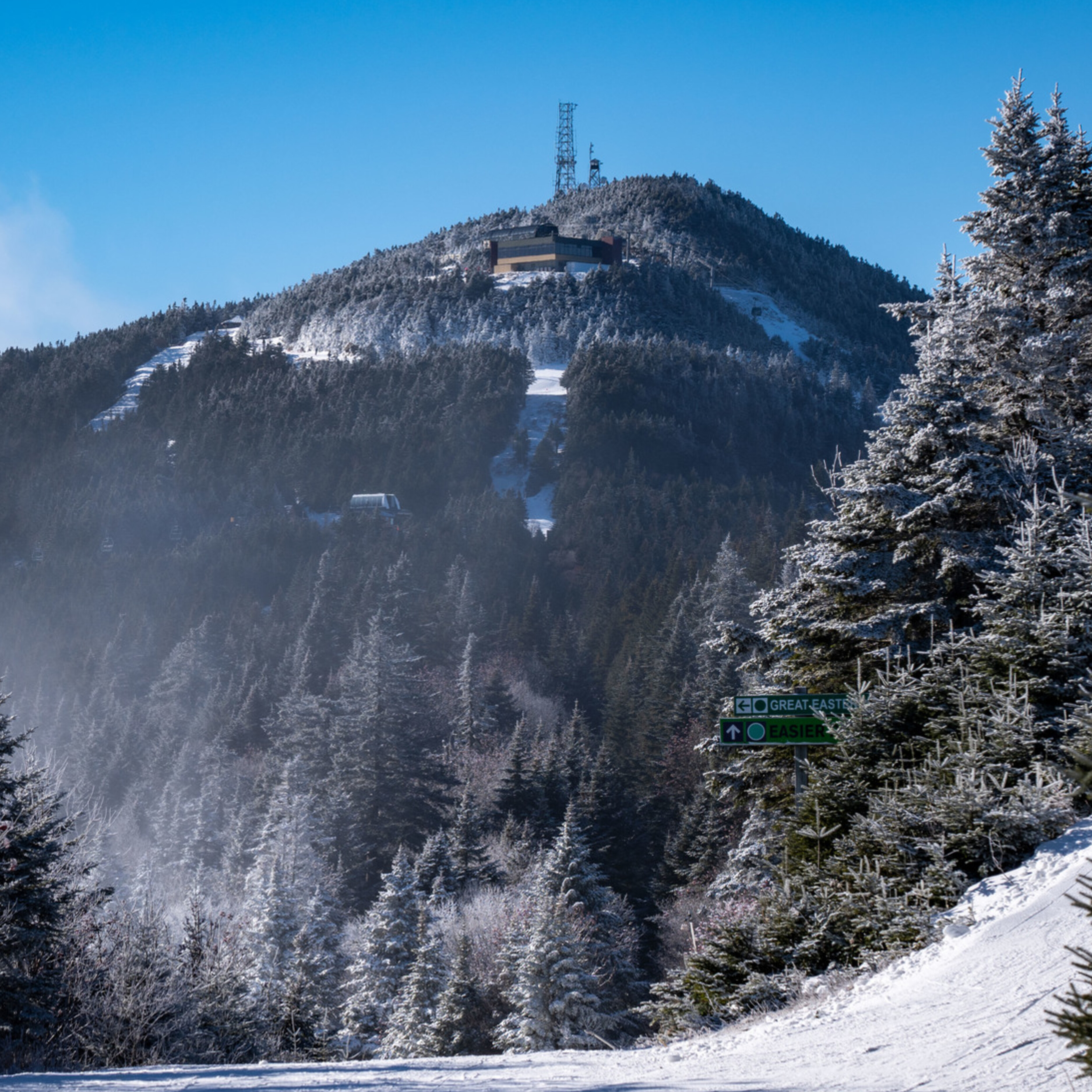 Snow-covered mountain with a building and communication tower on top. Ski signs visible.