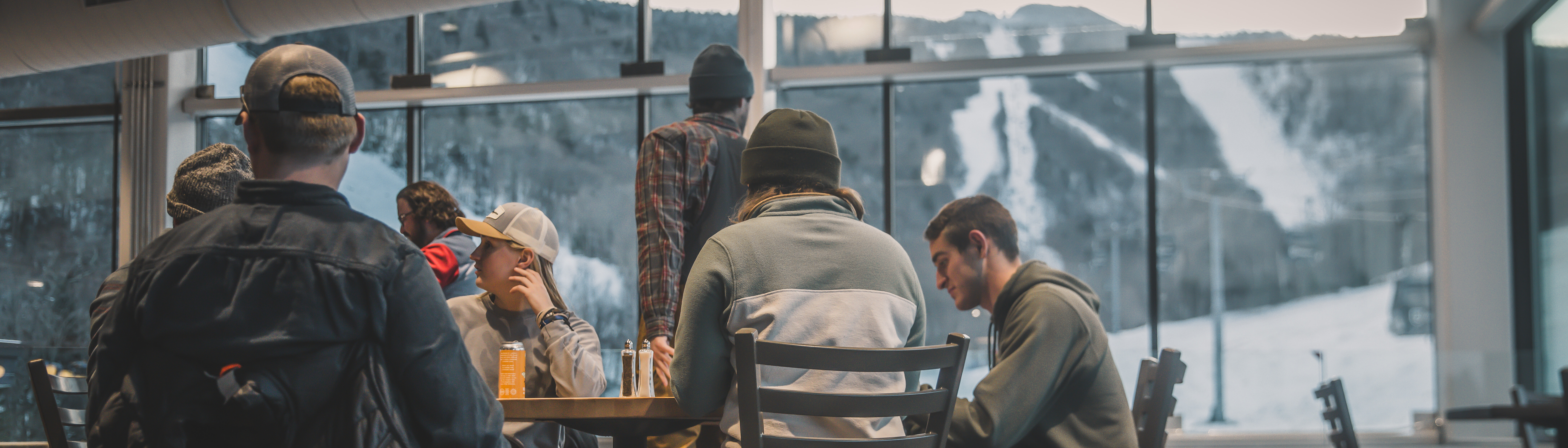 Group of people sitting at a table in a cafe with mountain views outside.