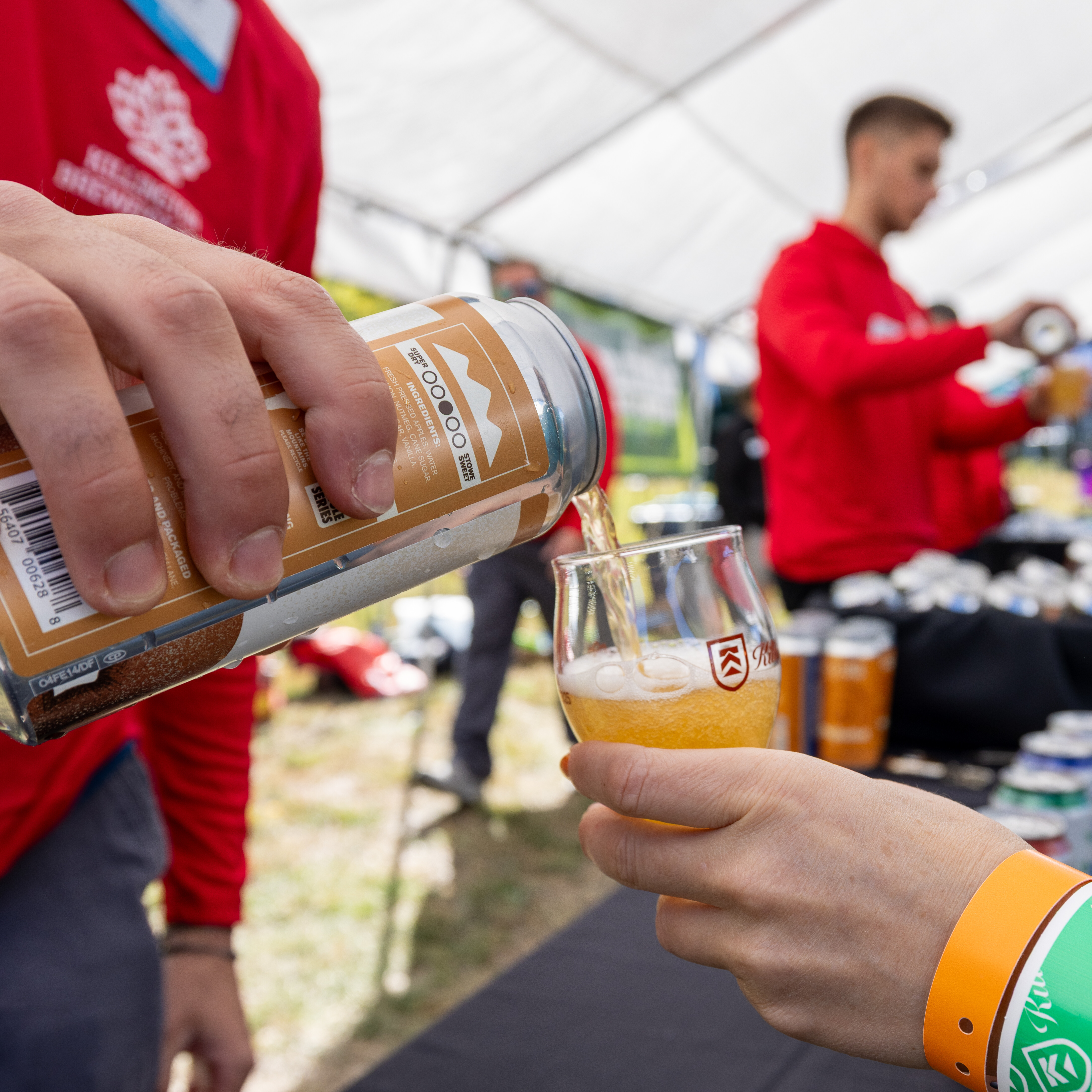 A person pours beer from a can into a tasting glass at a festival.