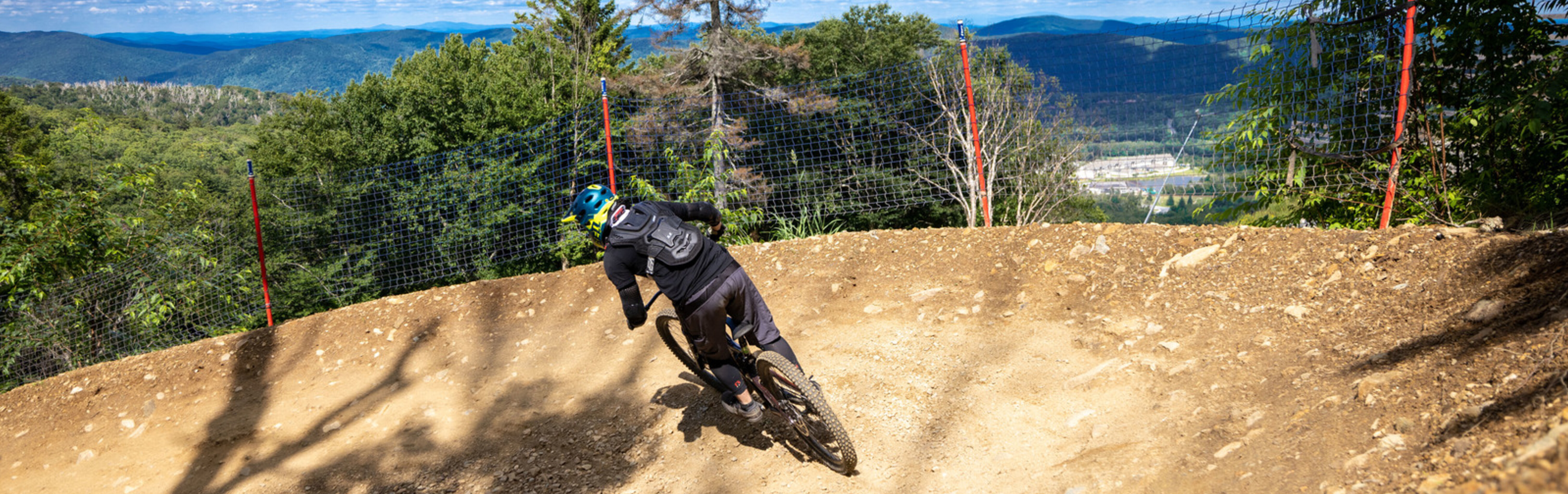 Mountain biker navigating a curve on a dirt trail with a scenic mountain backdrop.