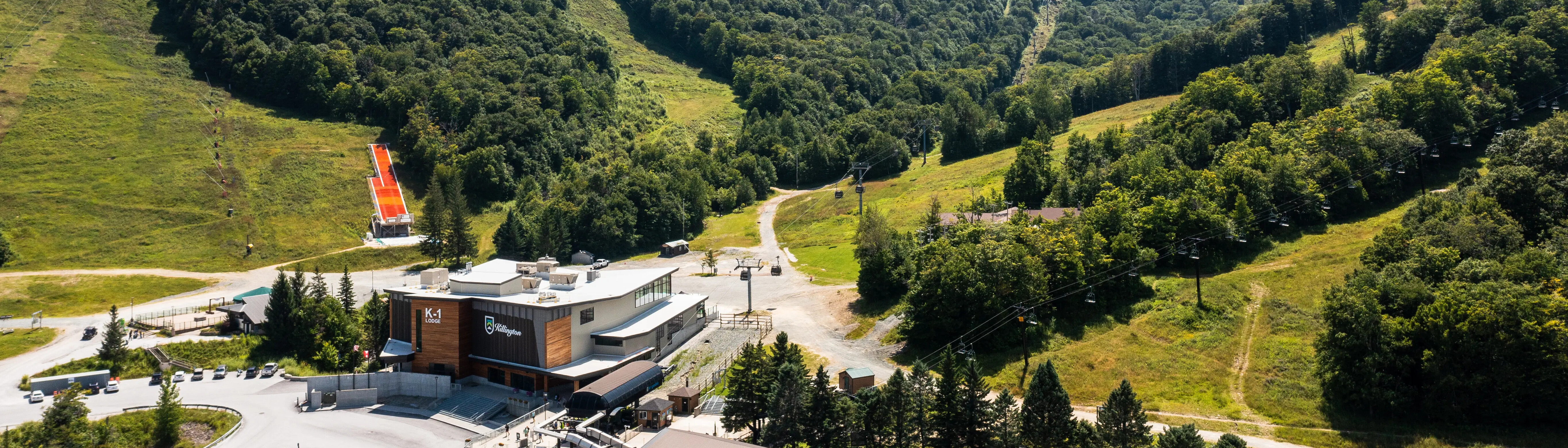Aerial view of a ski lodge and surrounding green hills with ski lifts.