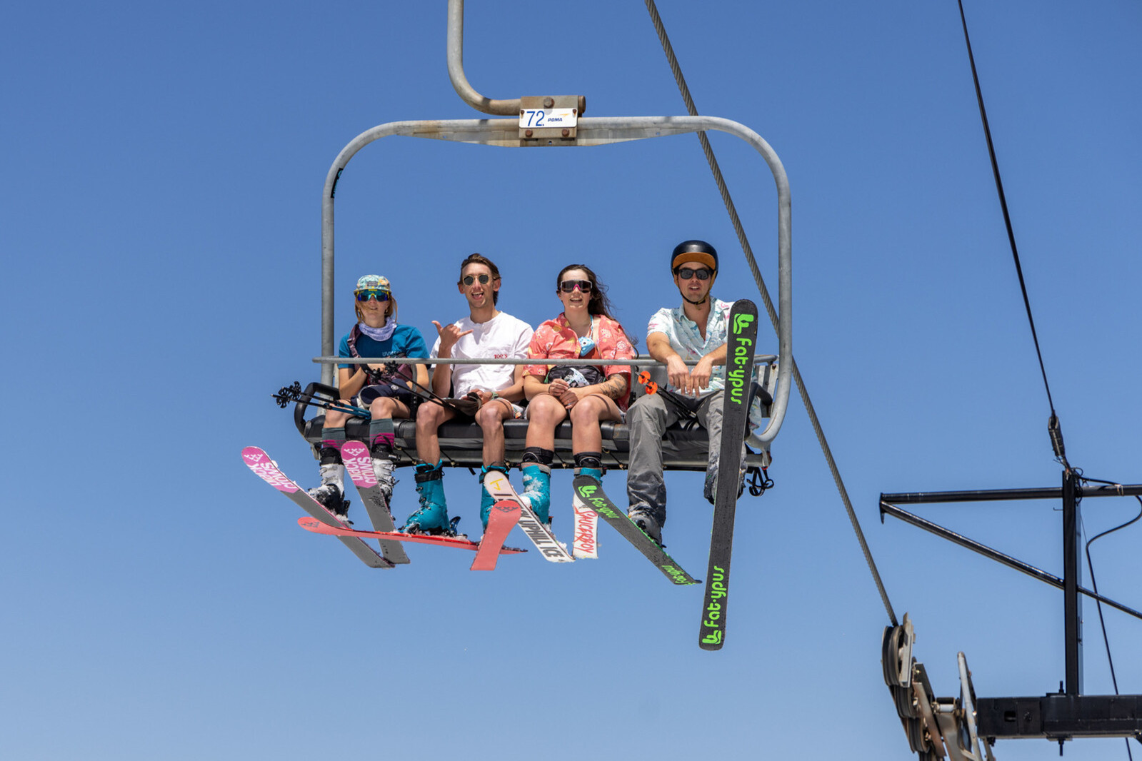 Four skiers on a chairlift against a clear blue sky.