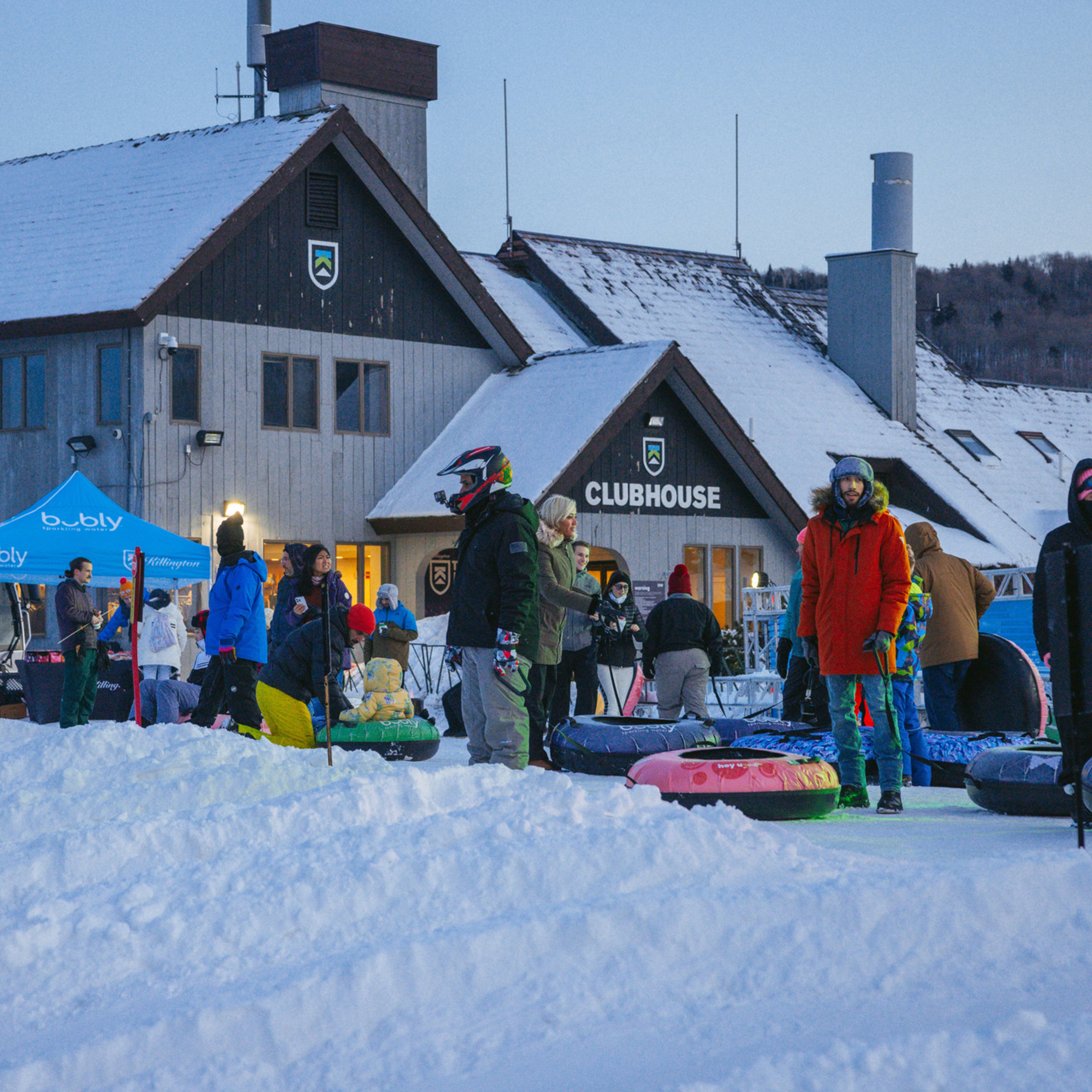 People gather in front of a snowy clubhouse, ready for tubing fun.