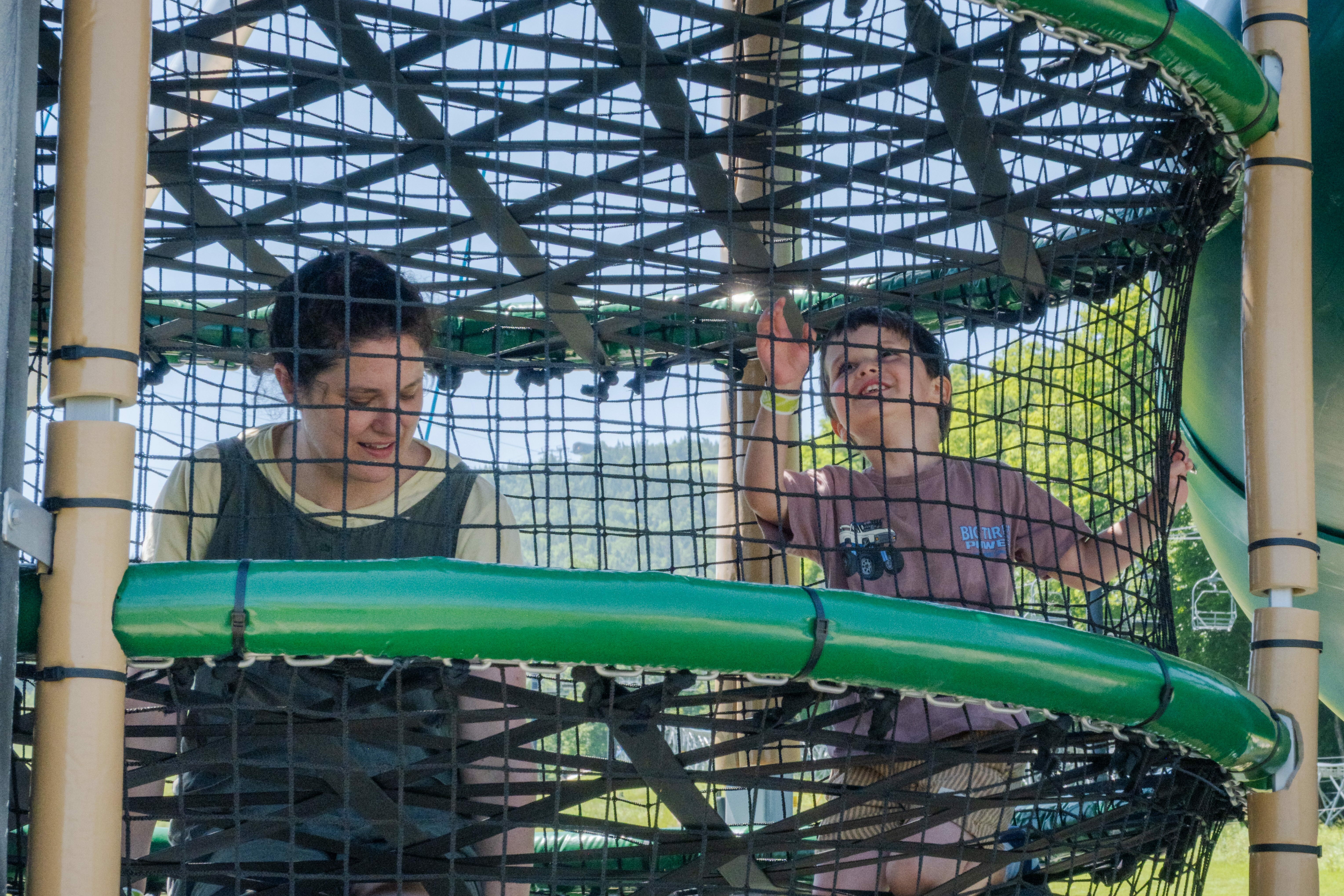 A woman and a young boy play together in a park's climbing structure.
