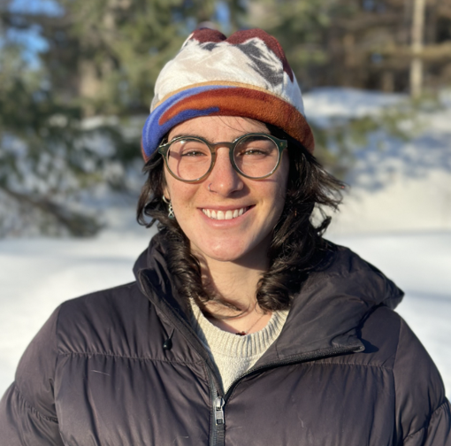 Smiling person in winter clothing and a colorful hat, standing in a snowy setting.