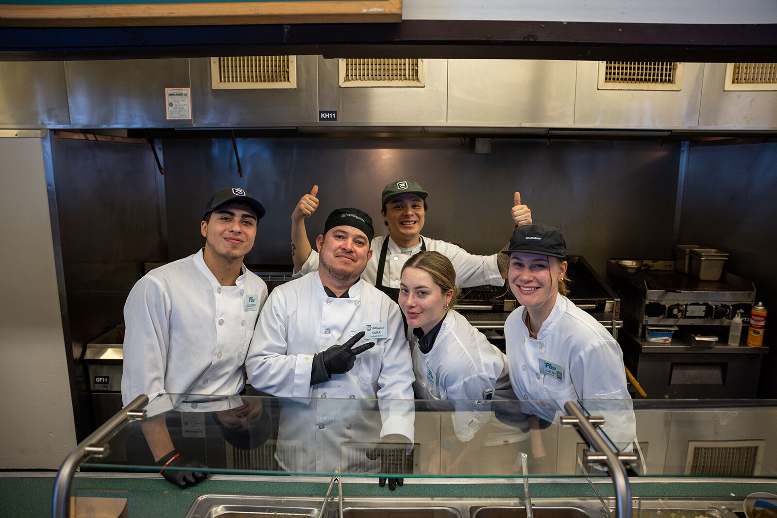 Five kitchen staff members pose together, smiling, in a restaurant kitchen.