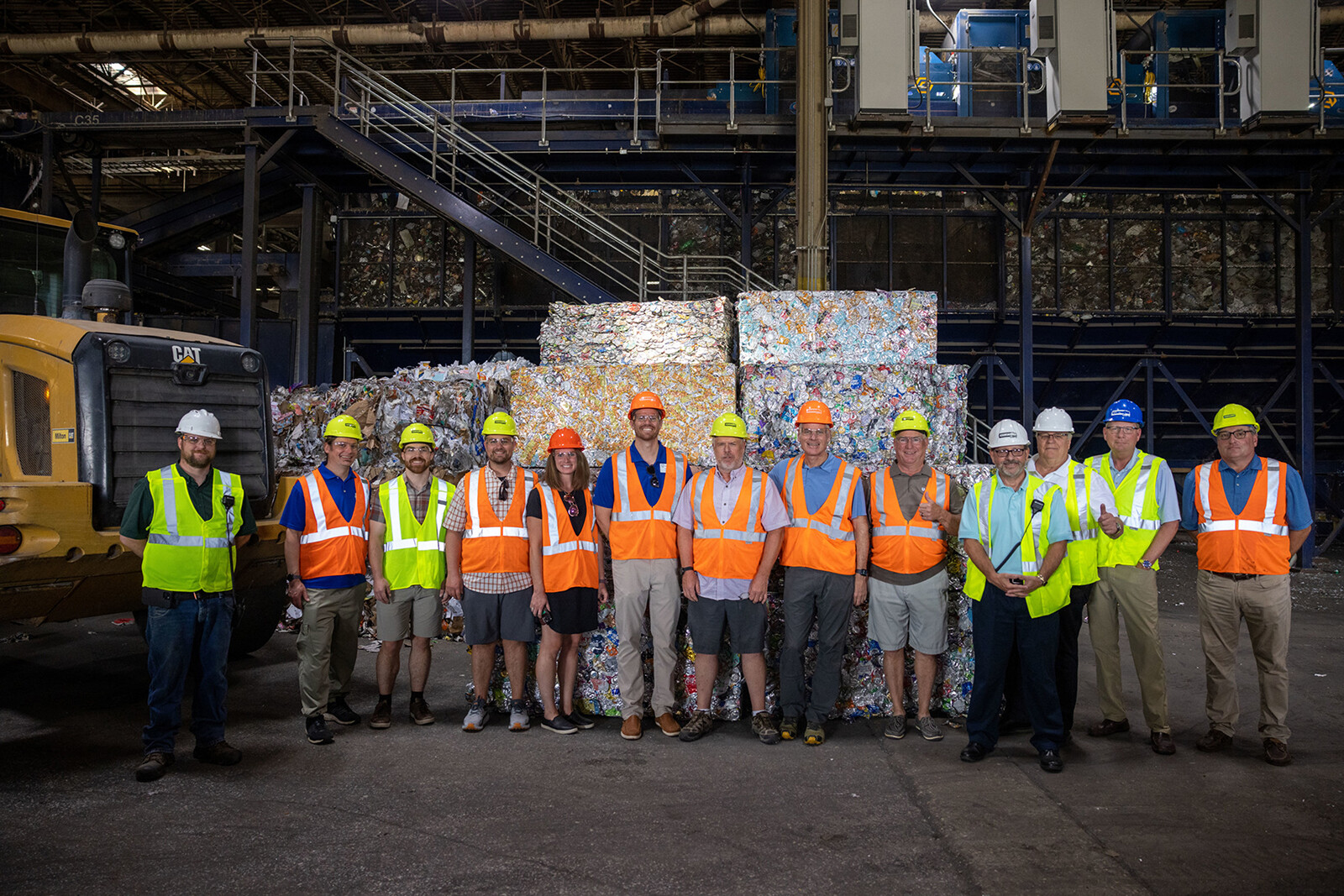 Group of people in safety vests and helmets standing in a recycling facility.