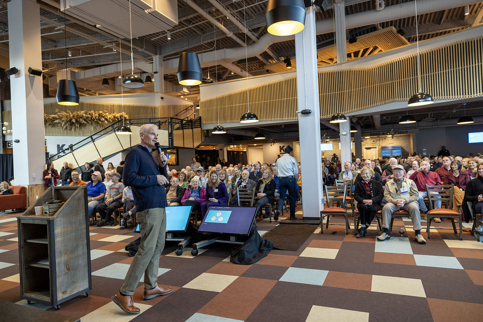 A speaker addresses a large audience in a modern venue.