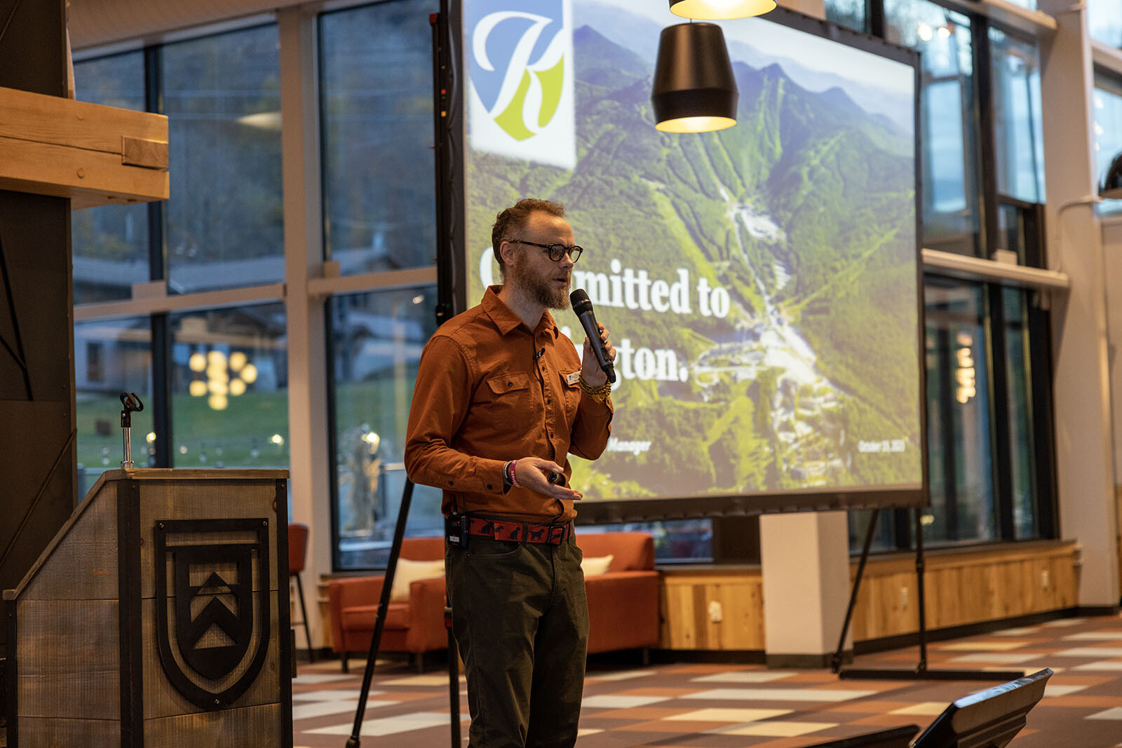A speaker presents in front of a large screen showcasing a scenic mountain view.