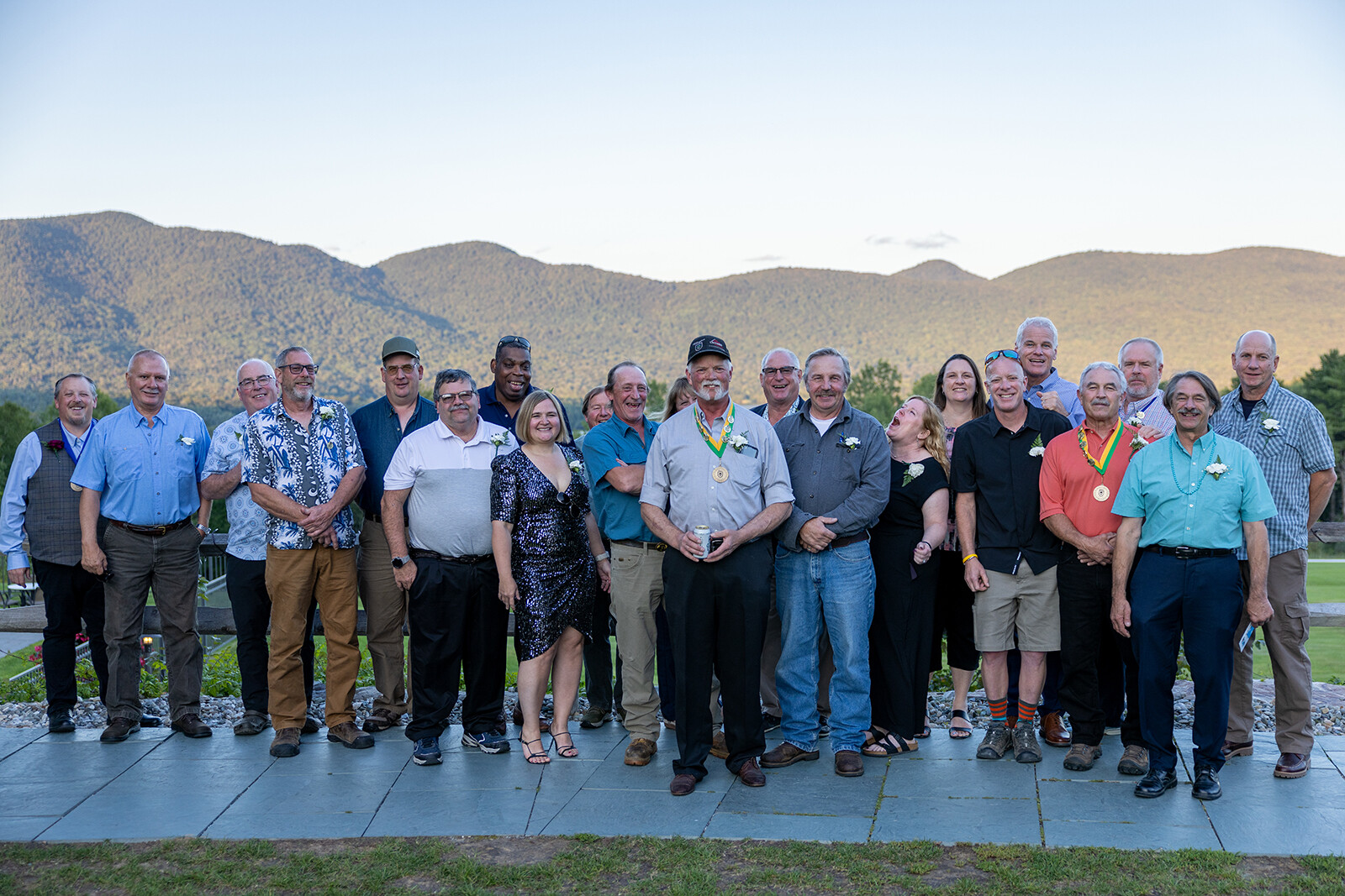 Group photo of smiling individuals in front of mountains, celebrating an event outdoors.
