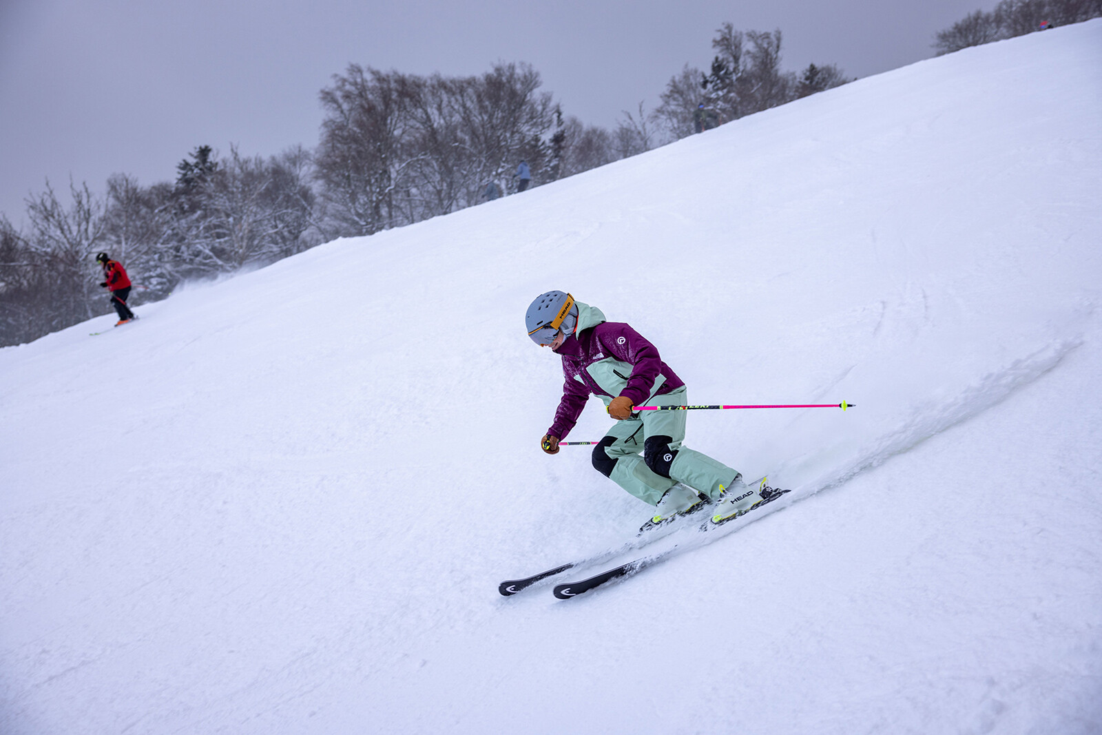 A skier in colorful gear navigates a snowy slope while another skier is seen in the background.