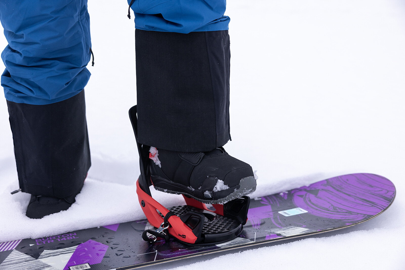 Close-up of a snowboard boot secured on a snowboard, surrounded by snow.