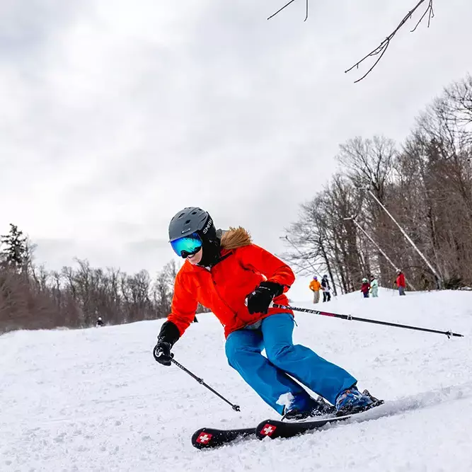 A skier in a red jacket and helmet navigates a snowy slope at Killington Mountain.