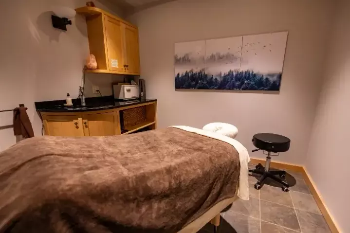 A serene massage room with a treatment table, artwork, and wooden storage.