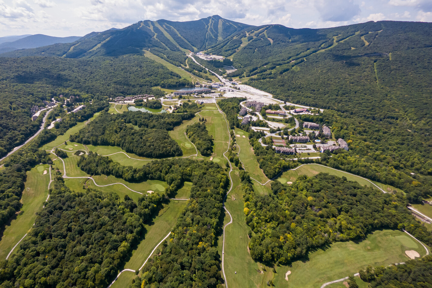 Aerial view of green hills, golf courses, and a ski resort in the mountains.