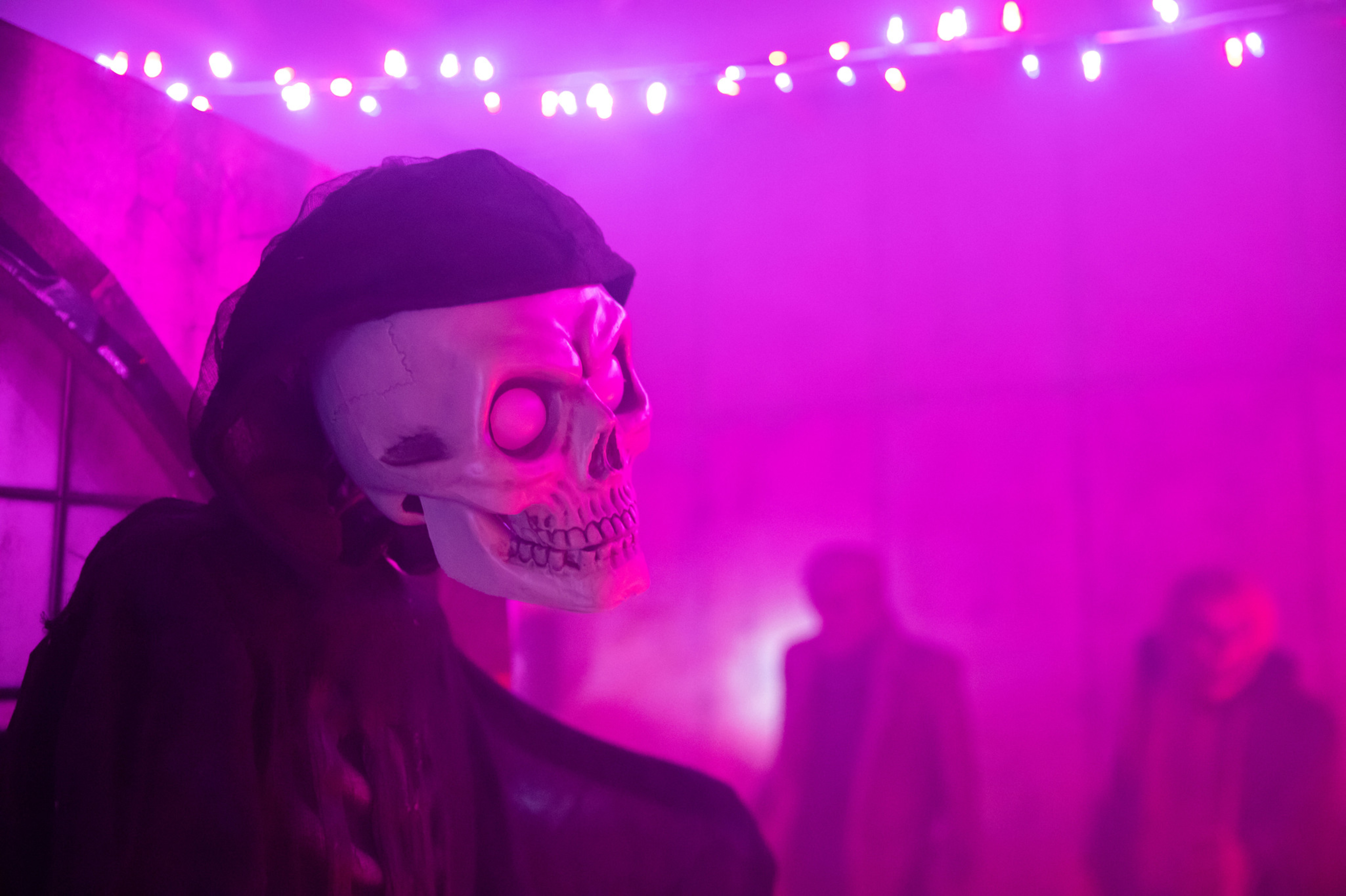 A skeleton figure in a dark cloak amidst fog and colorful lights.