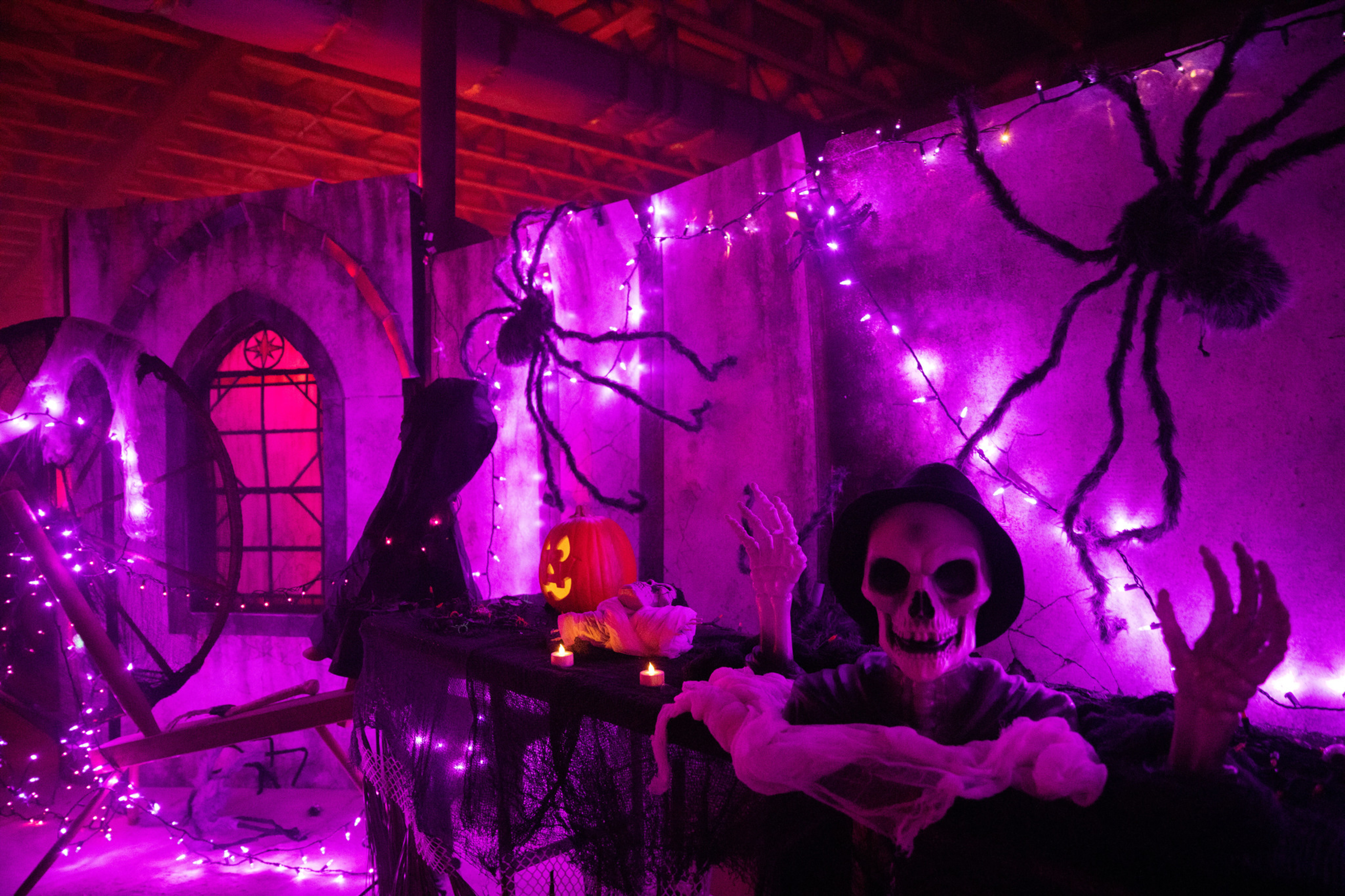 Spooky Halloween decor with a skeleton, pumpkin, purple lights, and spider decorations.
