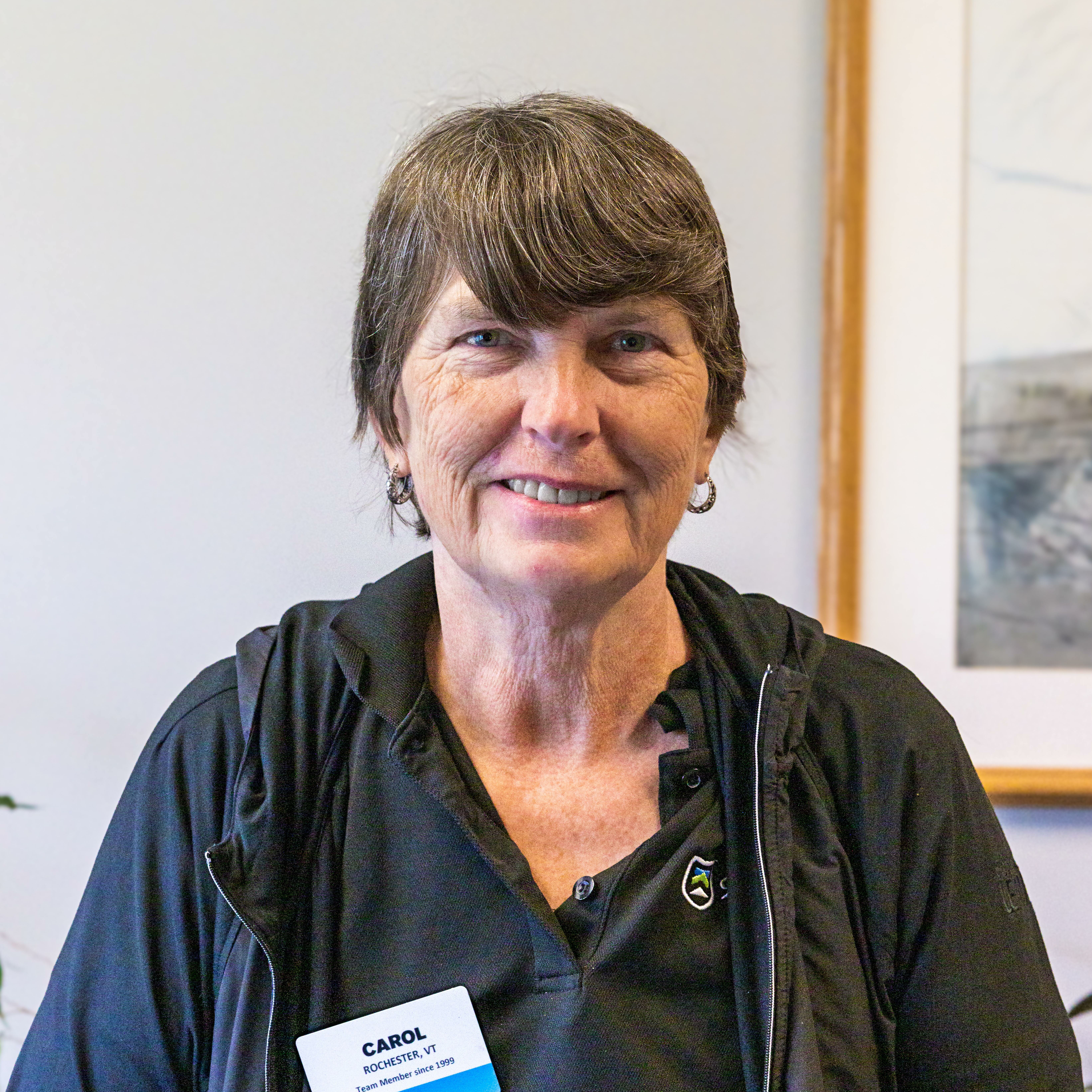 Smiling woman in a black shirt, wearing earrings and a name badge.