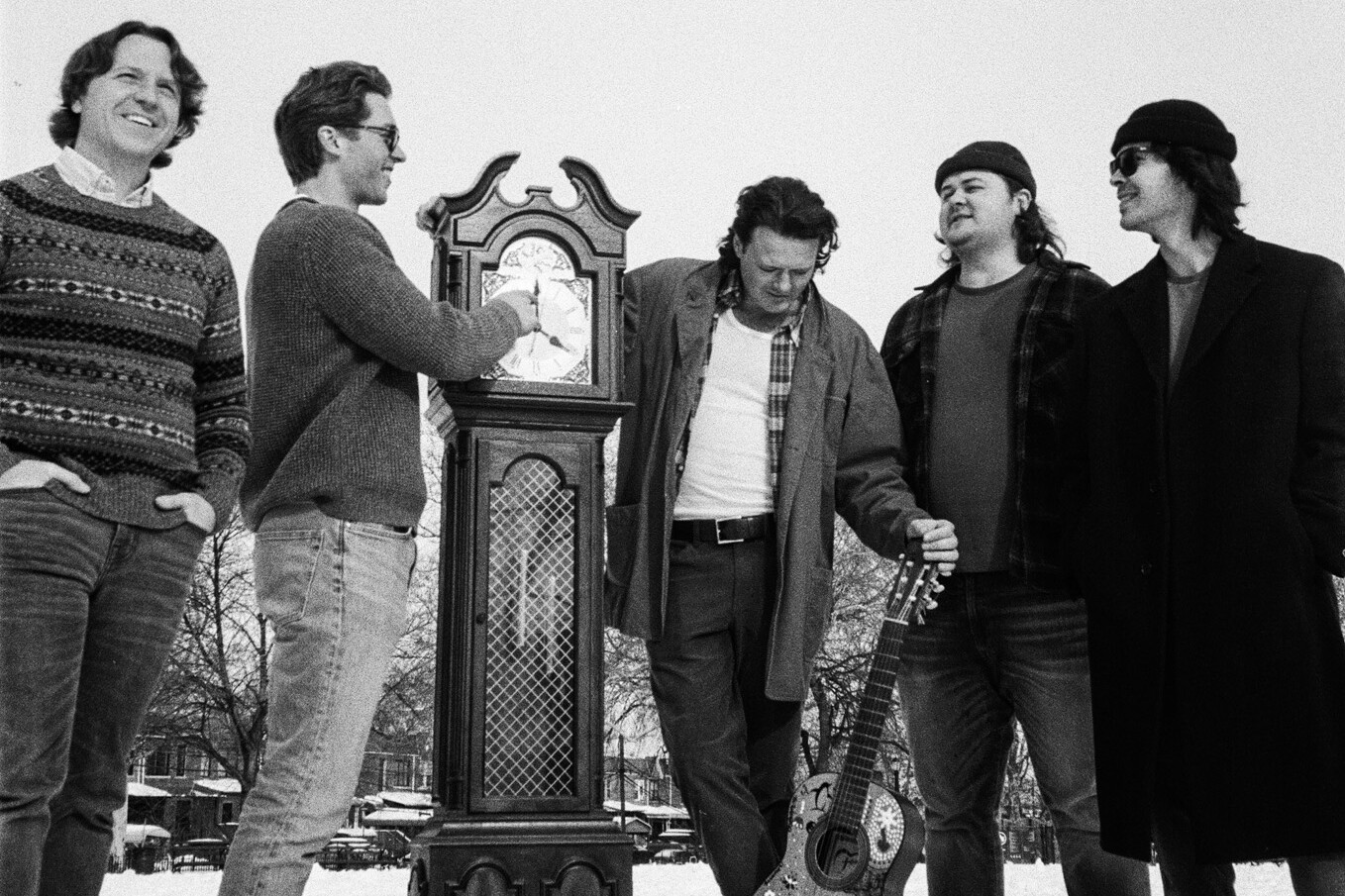 Five men gather around a vintage clock in a snowy outdoor setting.