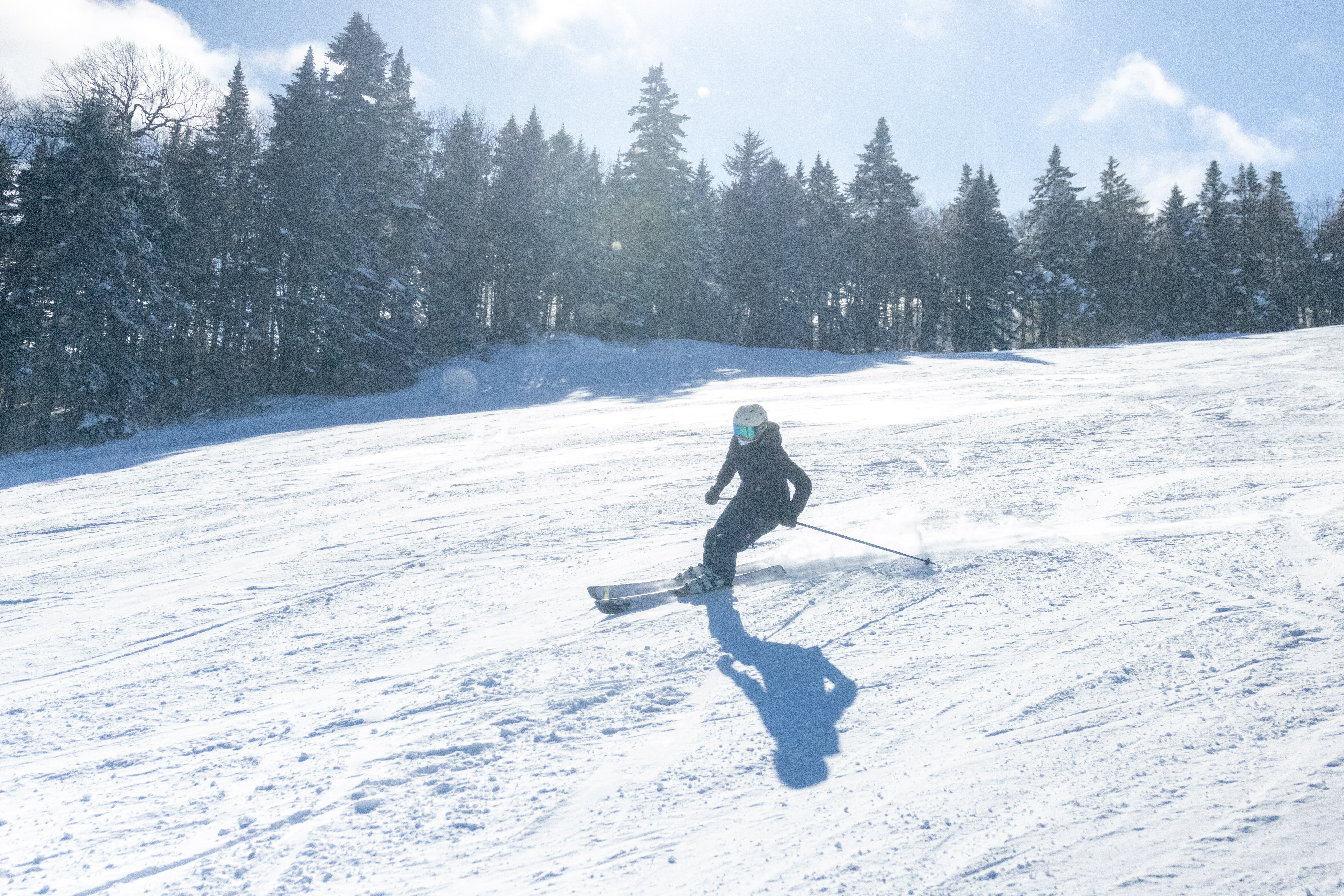 A skier in black gear glides down a snowy slope with trees in the background.