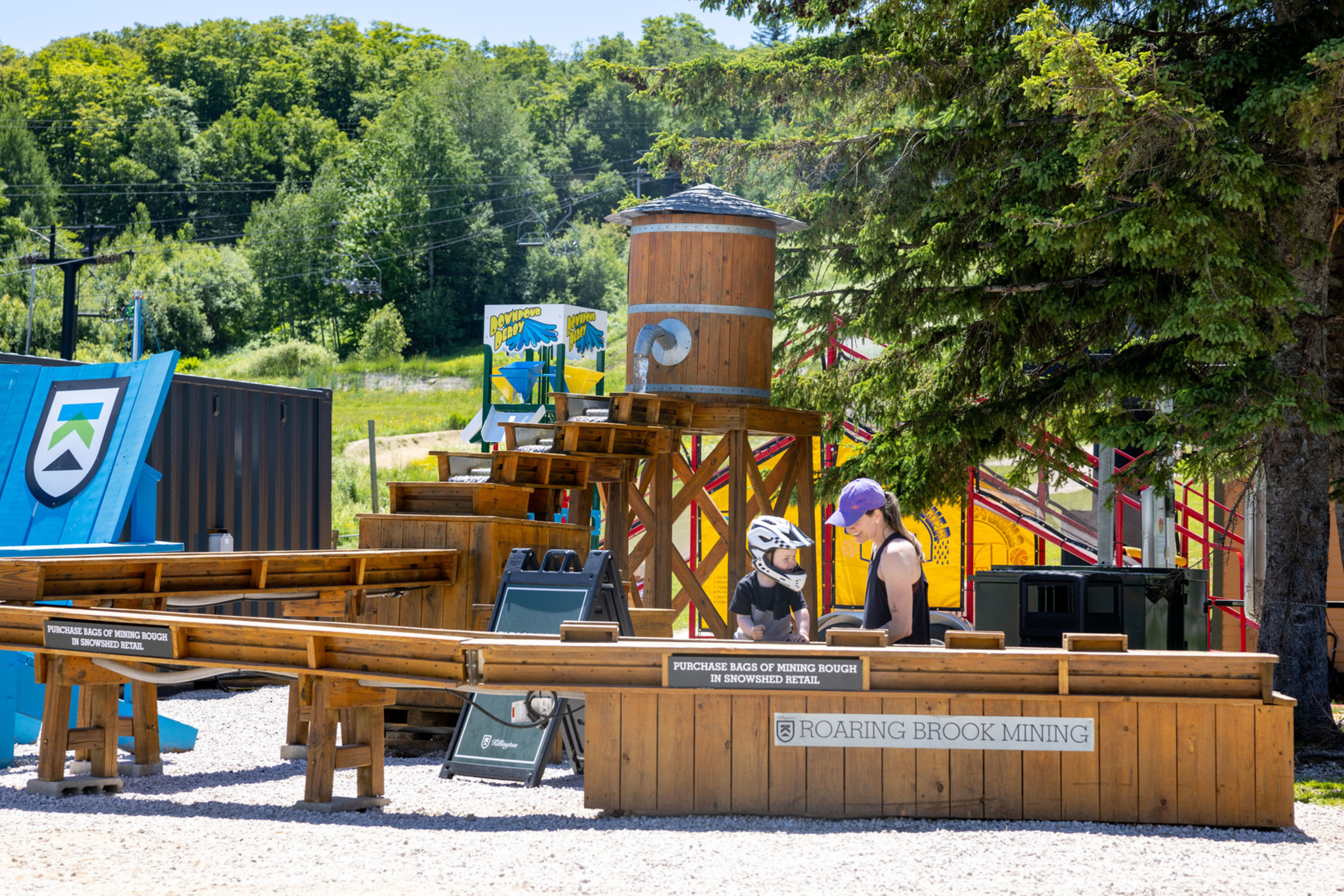 Children interact at a wooden mining activity area in a sunny outdoor setting.