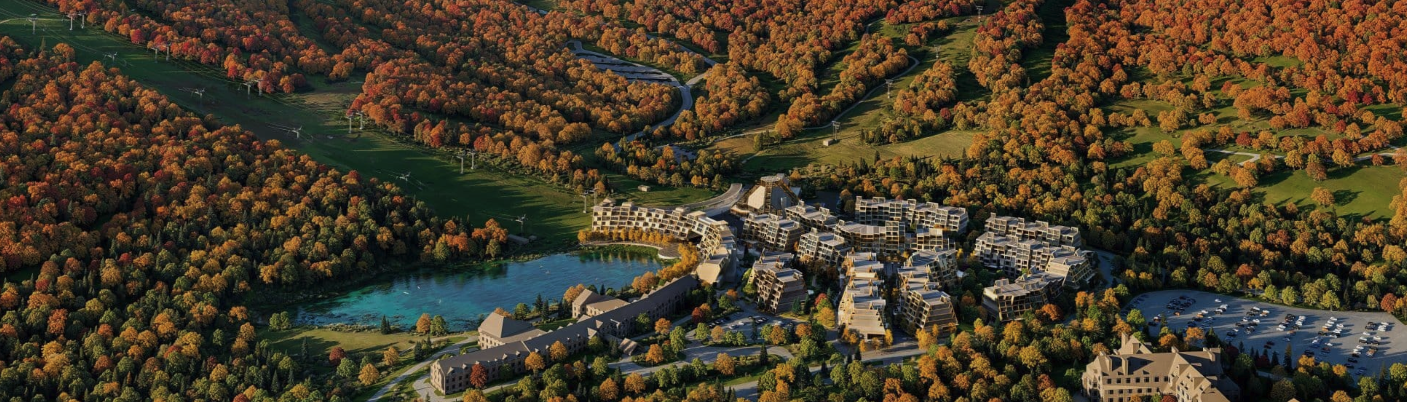 Aerial view of a resort surrounded by colorful autumn foliage and a serene lake.