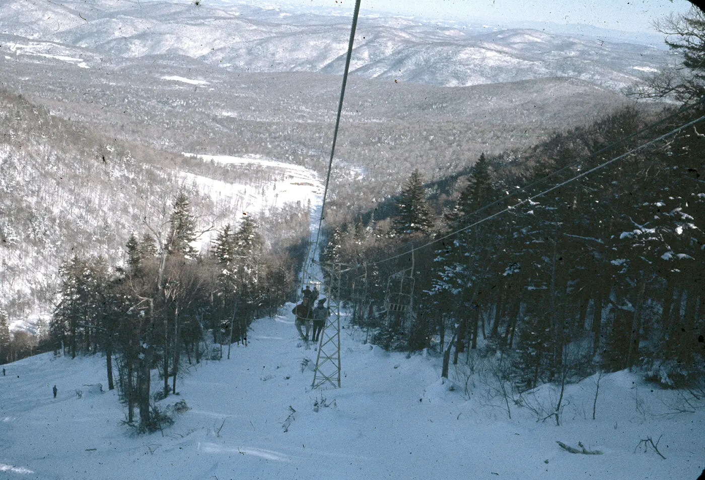 Ski lift overlooking a snowy mountain landscape with trees and hills in the distance.