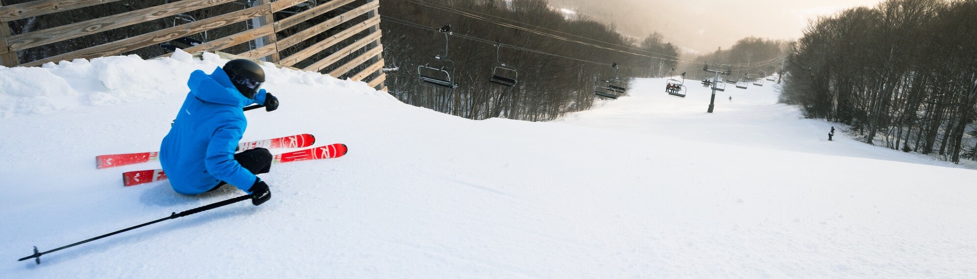 A skier in a blue jacket descends a snowy slope near a ski lift.