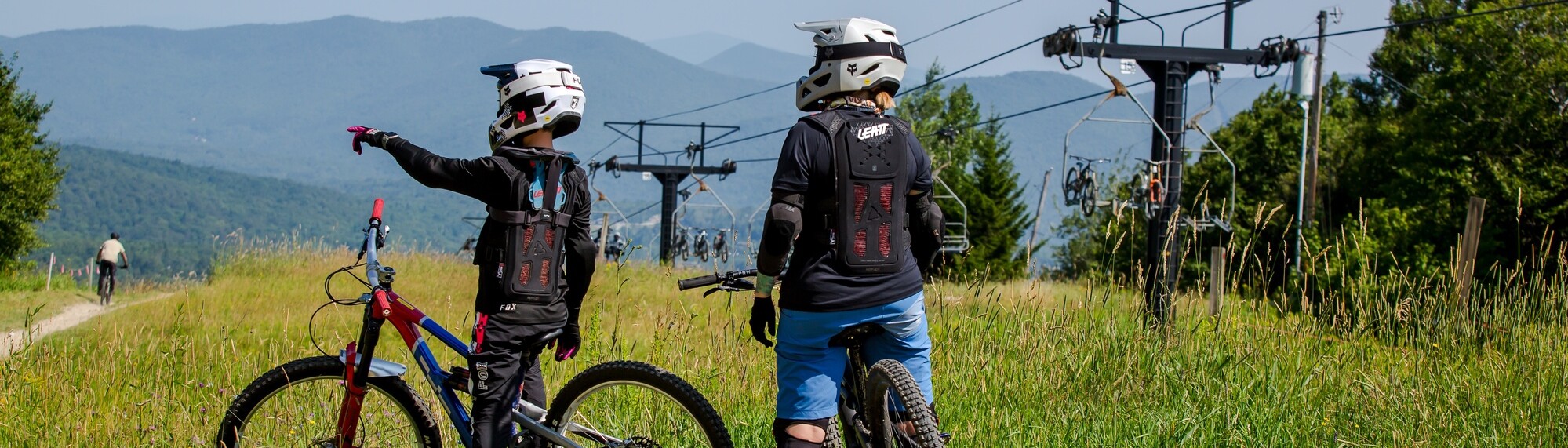 Two kids on bikes look towards a ski lift in a mountain landscape.