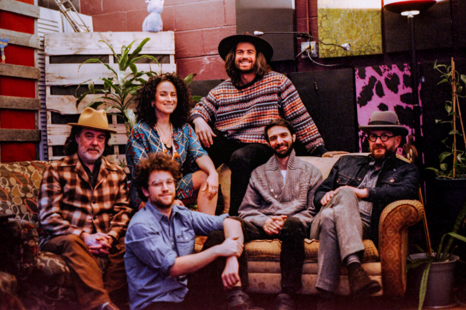 A group of six people sitting on a couch in a cozy, plant-filled space.