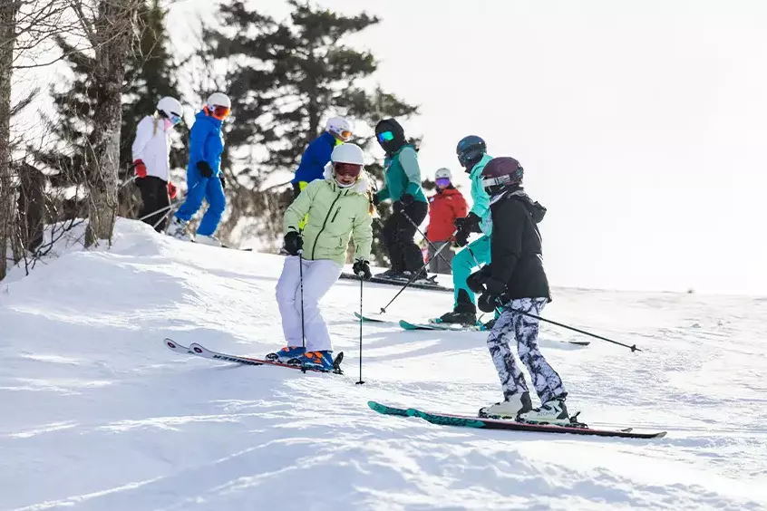 Skiers of various skill levels navigating a snowy slope on a sunny day.